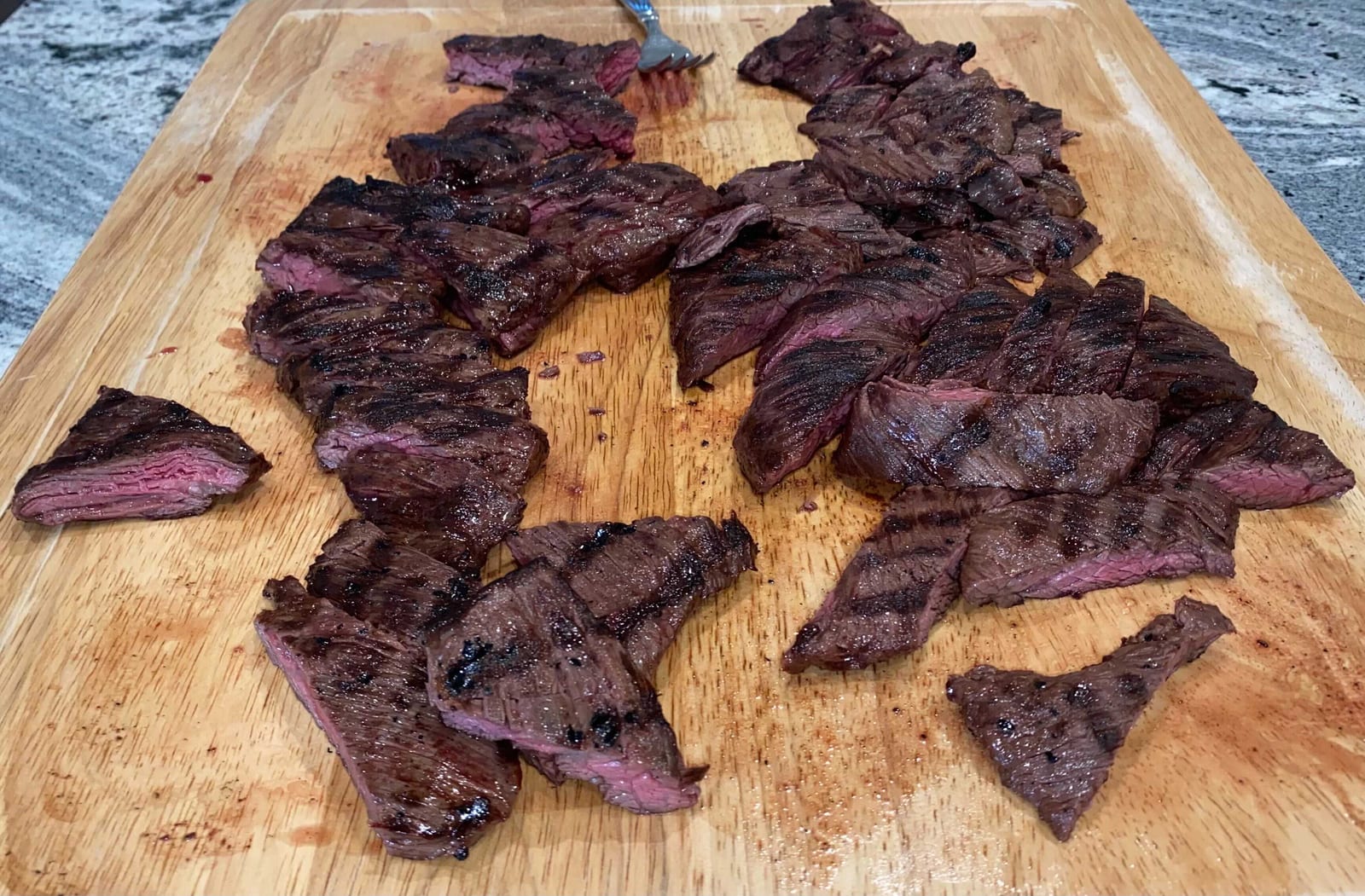 Grilled skirt steak cut across the grain into short strips on a wooden board.