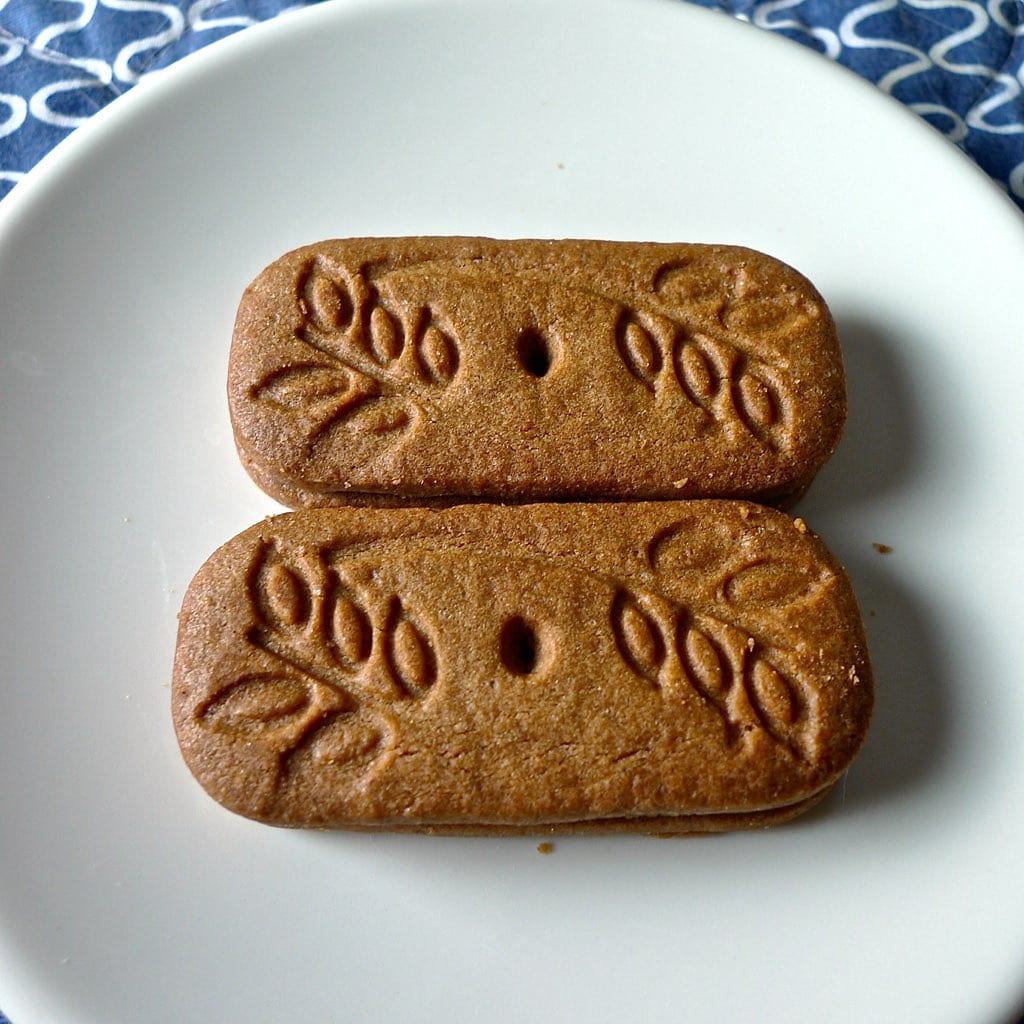Two embossed rectangular speculoos biscuits on a white plate beside a blue patterned cloth.