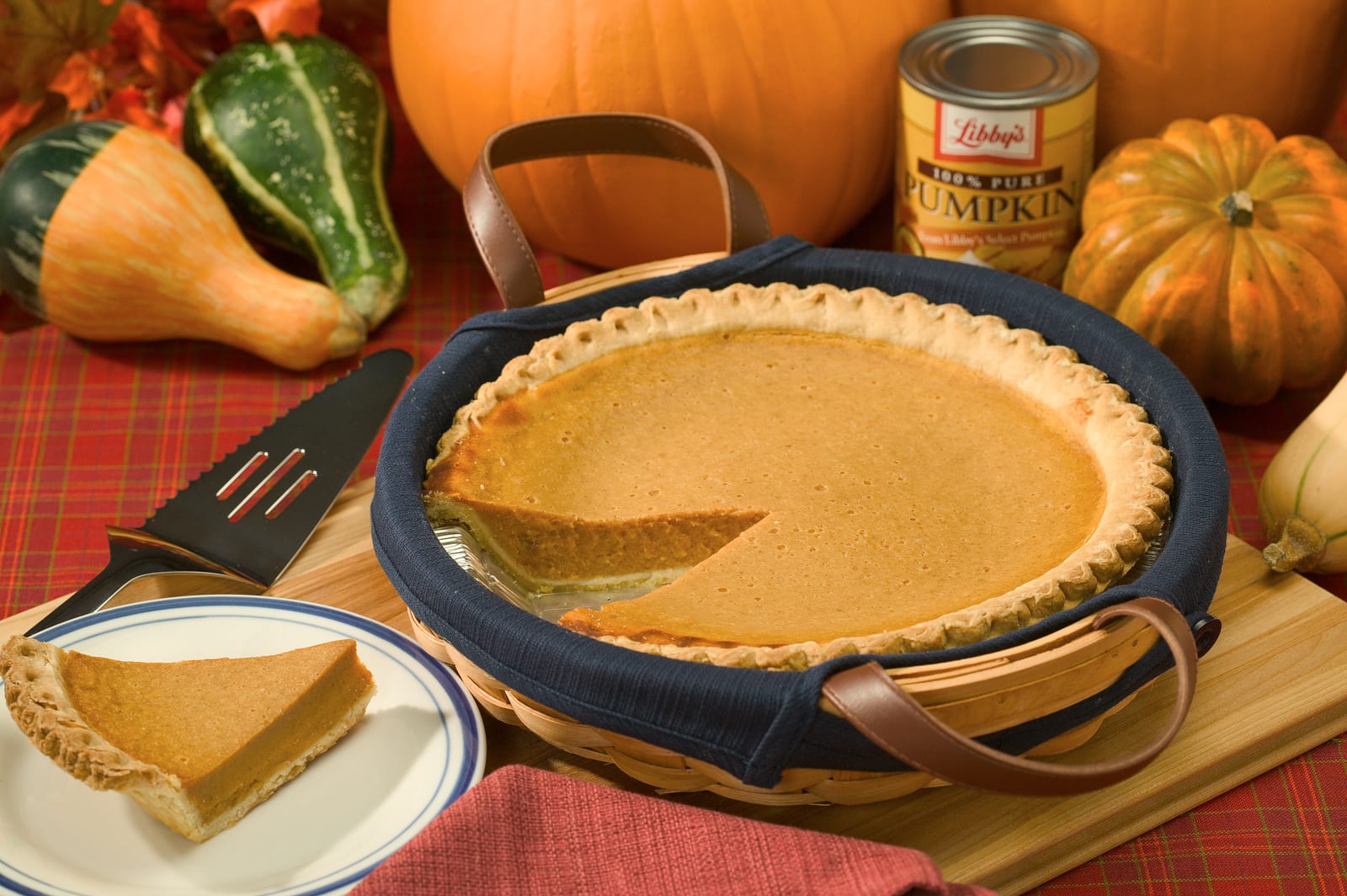 A whole pumpkin pie with one slice removed, set beside pumpkins and a serving plate.