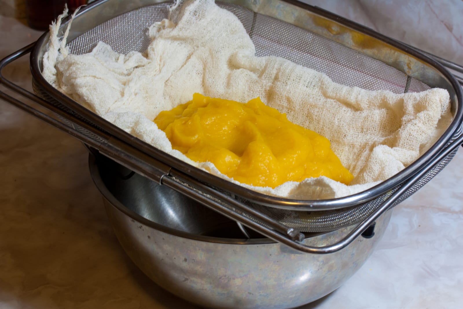 Bright pumpkin puree draining in cheesecloth set inside a mesh strainer.