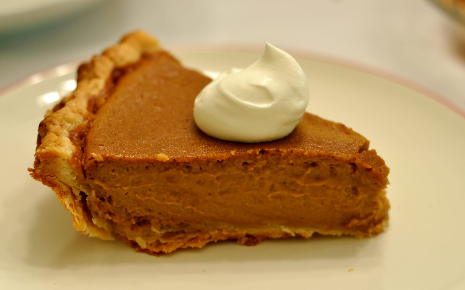 A slice of pumpkin pie topped with whipped cream on a white plate.