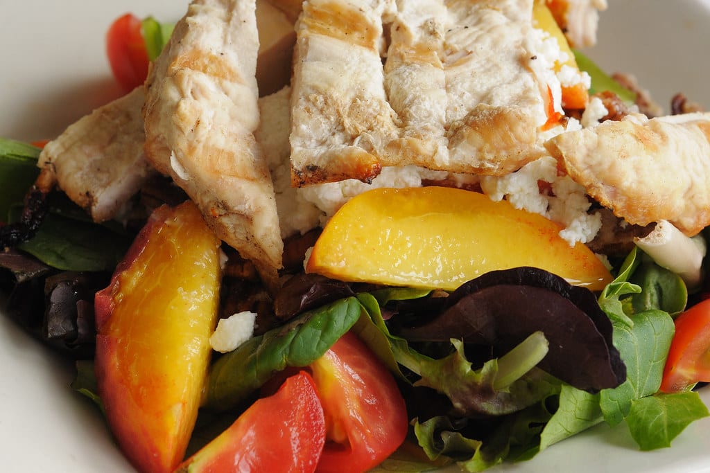 Grilled chicken and ripe peach wedges arranged over summer greens.