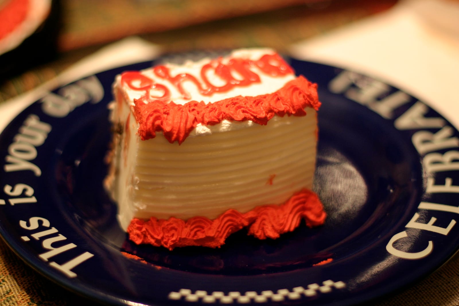 A small rectangular ice cream cake frosted white and red on a dark blue plate.