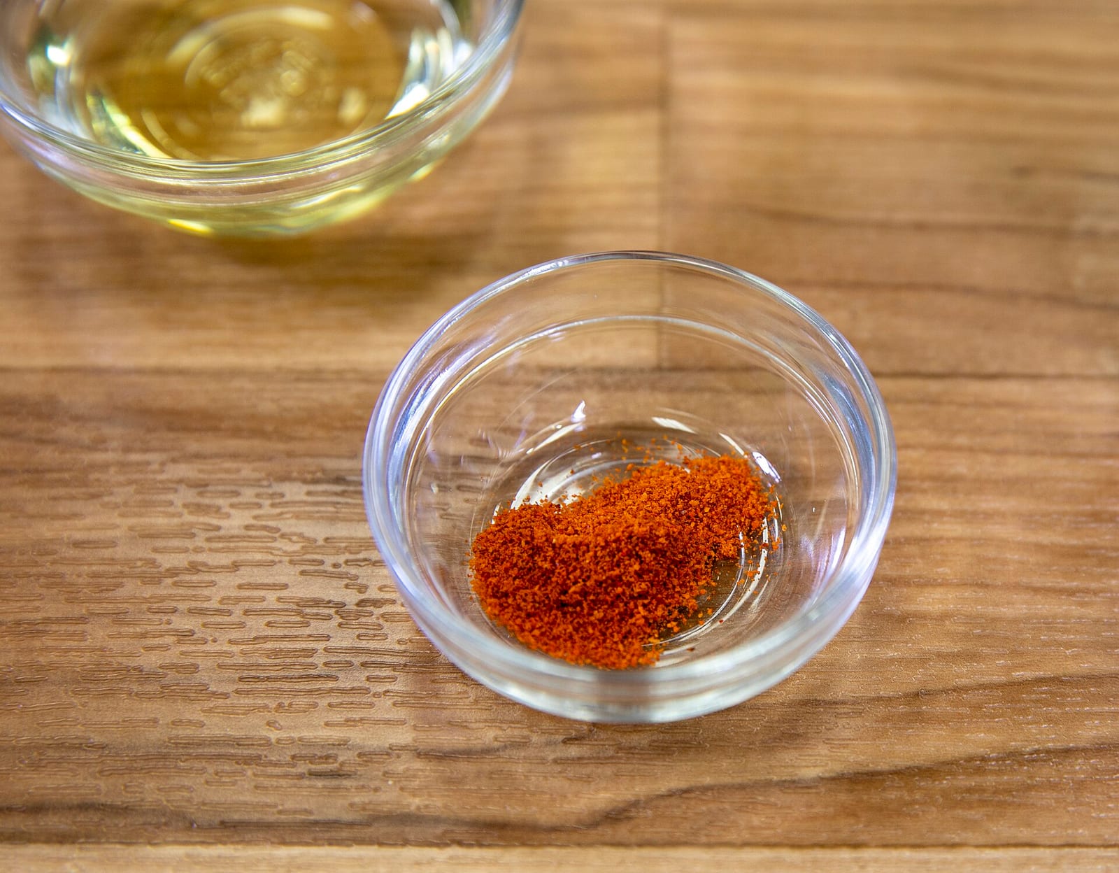 Ground cayenne pepper in a small glass bowl on a wooden work surface.