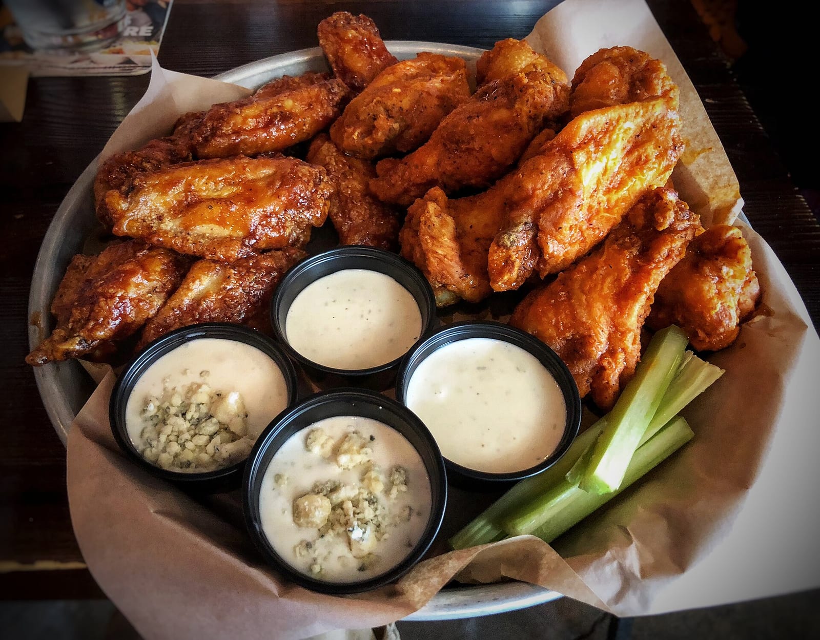 A large tray of crisp chicken wings arranged around cups of creamy dip and celery sticks.