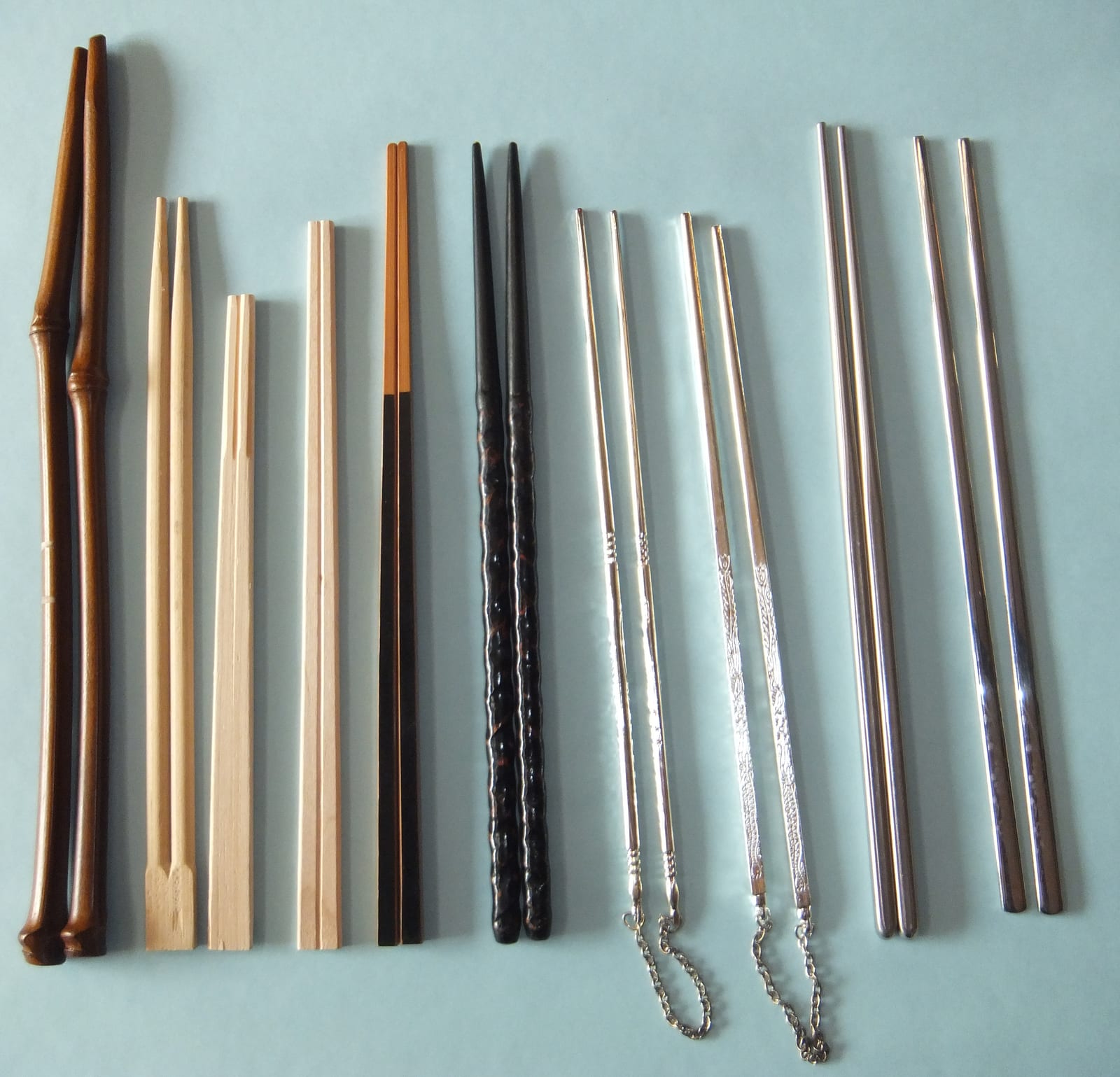Japanese, Chinese, and Korean chopsticks arranged in parallel on a pale surface.