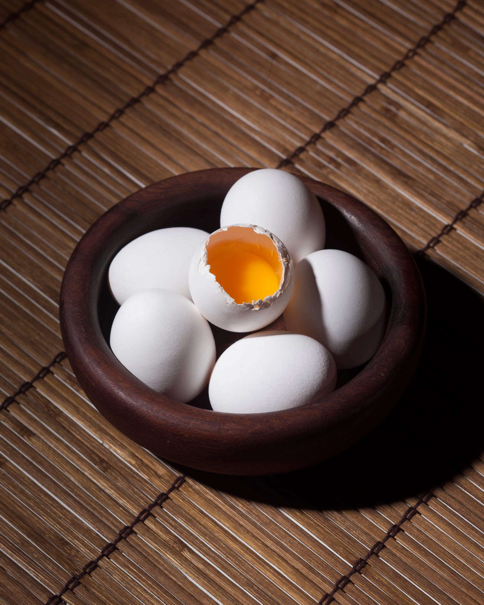 Brown and white eggs gathered in a ceramic bowl with one cracked shell showing a bright yolk.