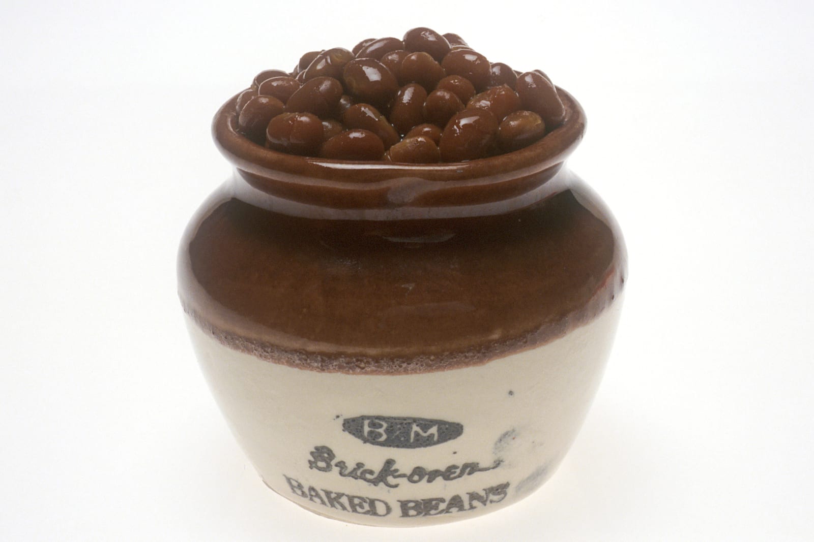 Glossy brown baked beans heaped in a cream and brown stoneware bean pot.