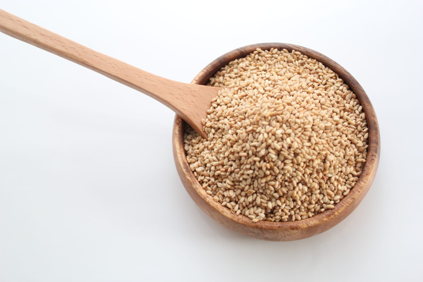 Toasted white sesame seeds in a wooden bowl with a wooden spoon.