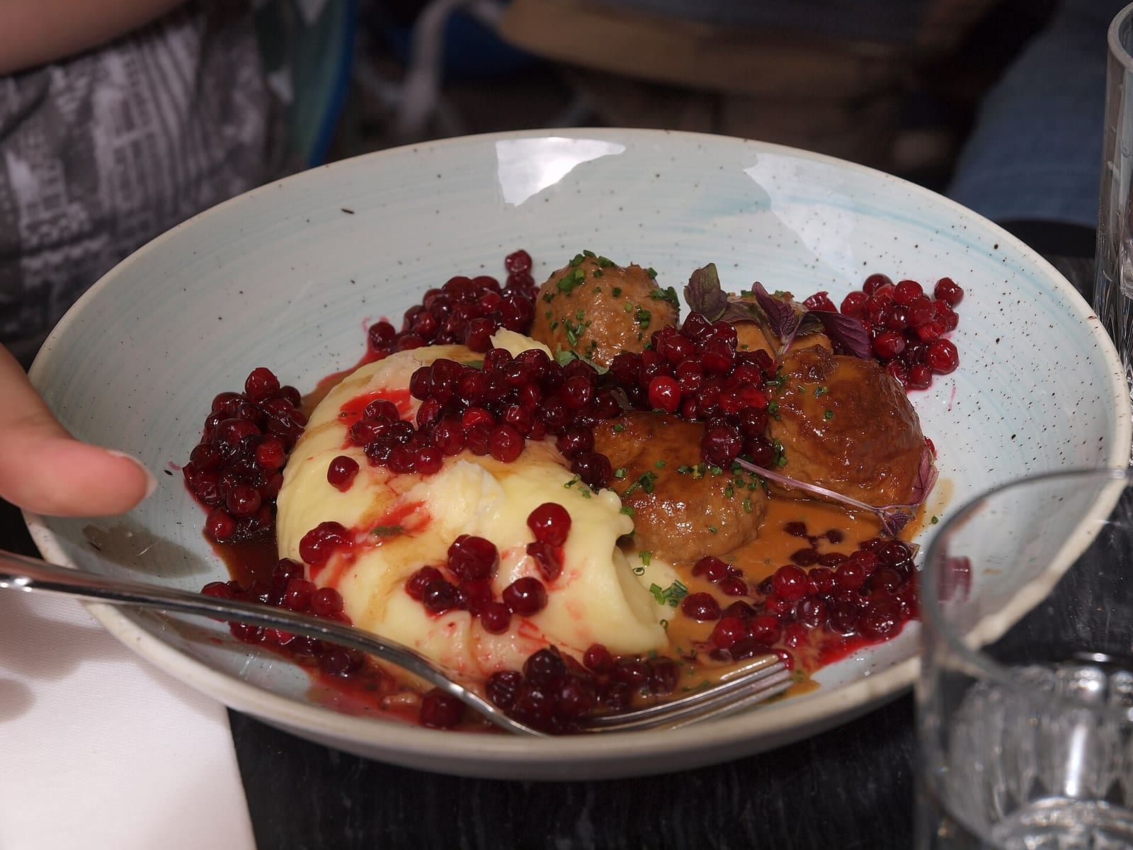 A plate of Swedish meatballs with potatoes, lingonberries, cucumber, and creamy sauce.