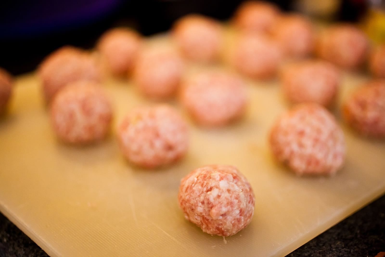 Hands shaping small Swedish meatballs on a tray before cooking.