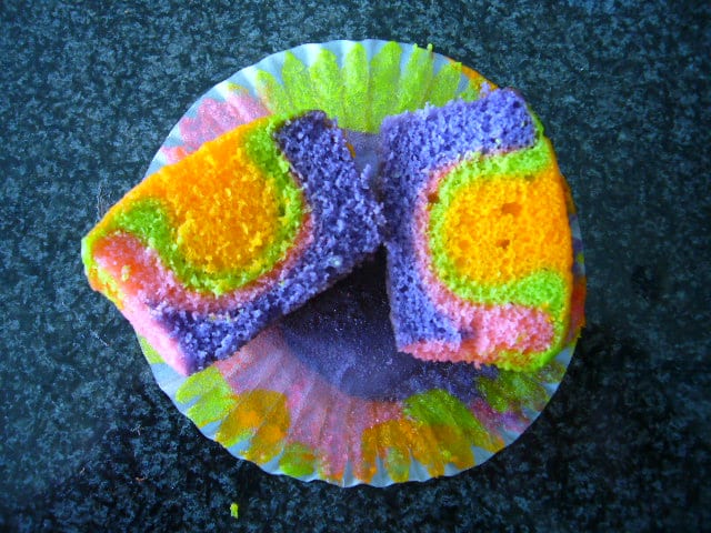 A rainbow-colored cupcake split open to show vivid purple, green, orange, and pink cake.