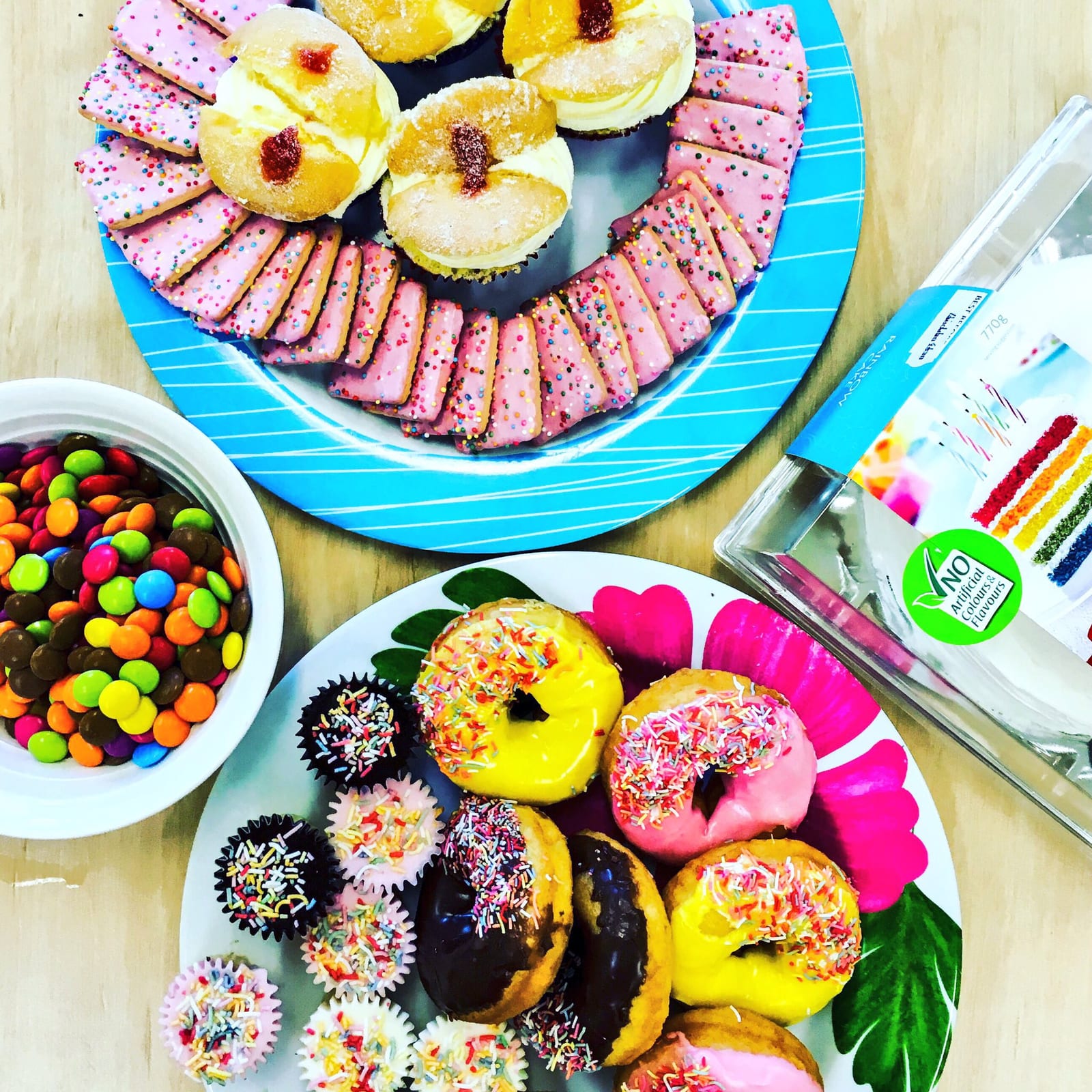 A colorful table of cupcakes, doughnuts, iced biscuits, sprinkles, and candy.