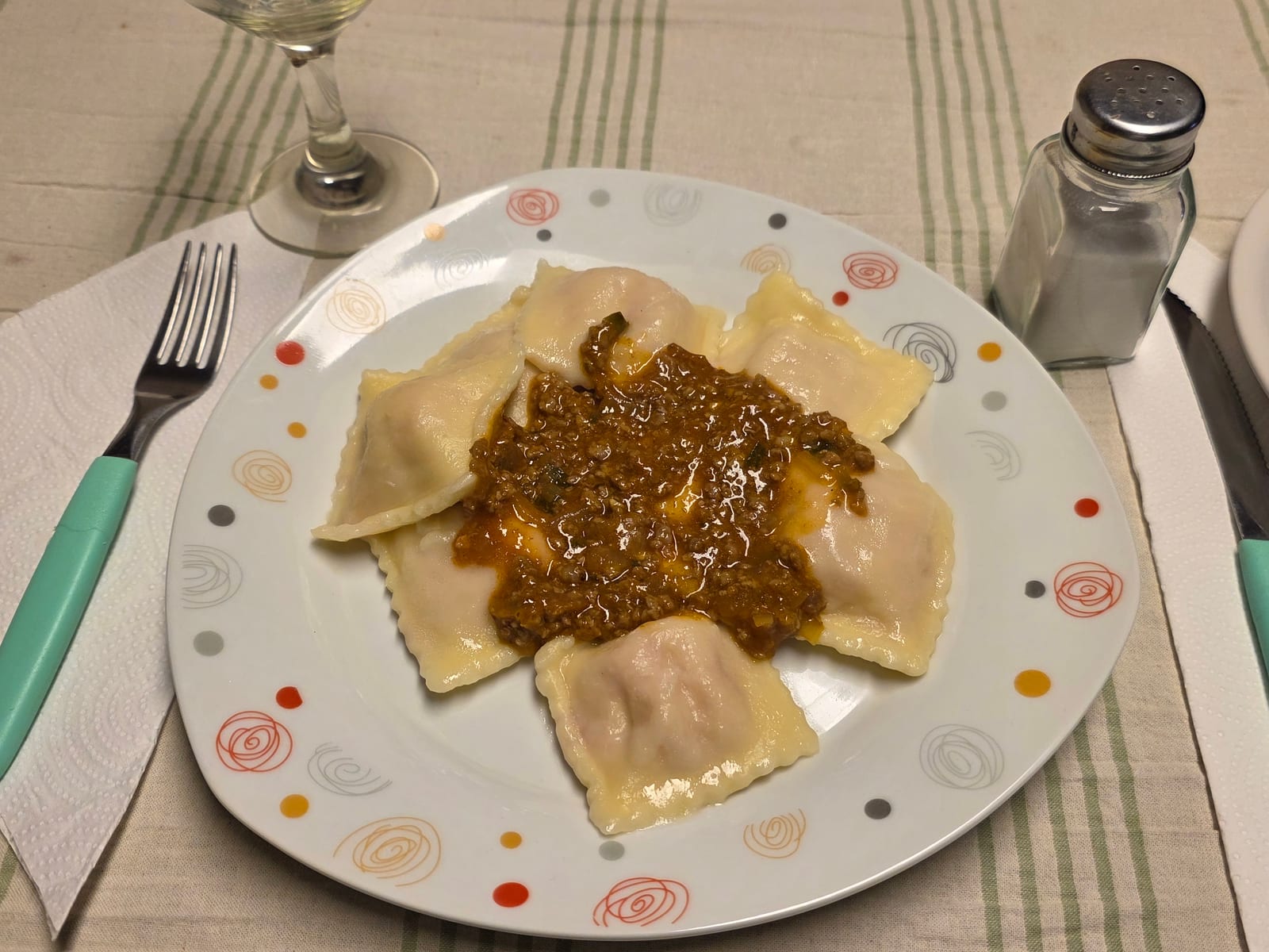Large square ravioli on a plate under a spoonful of meat sauce.