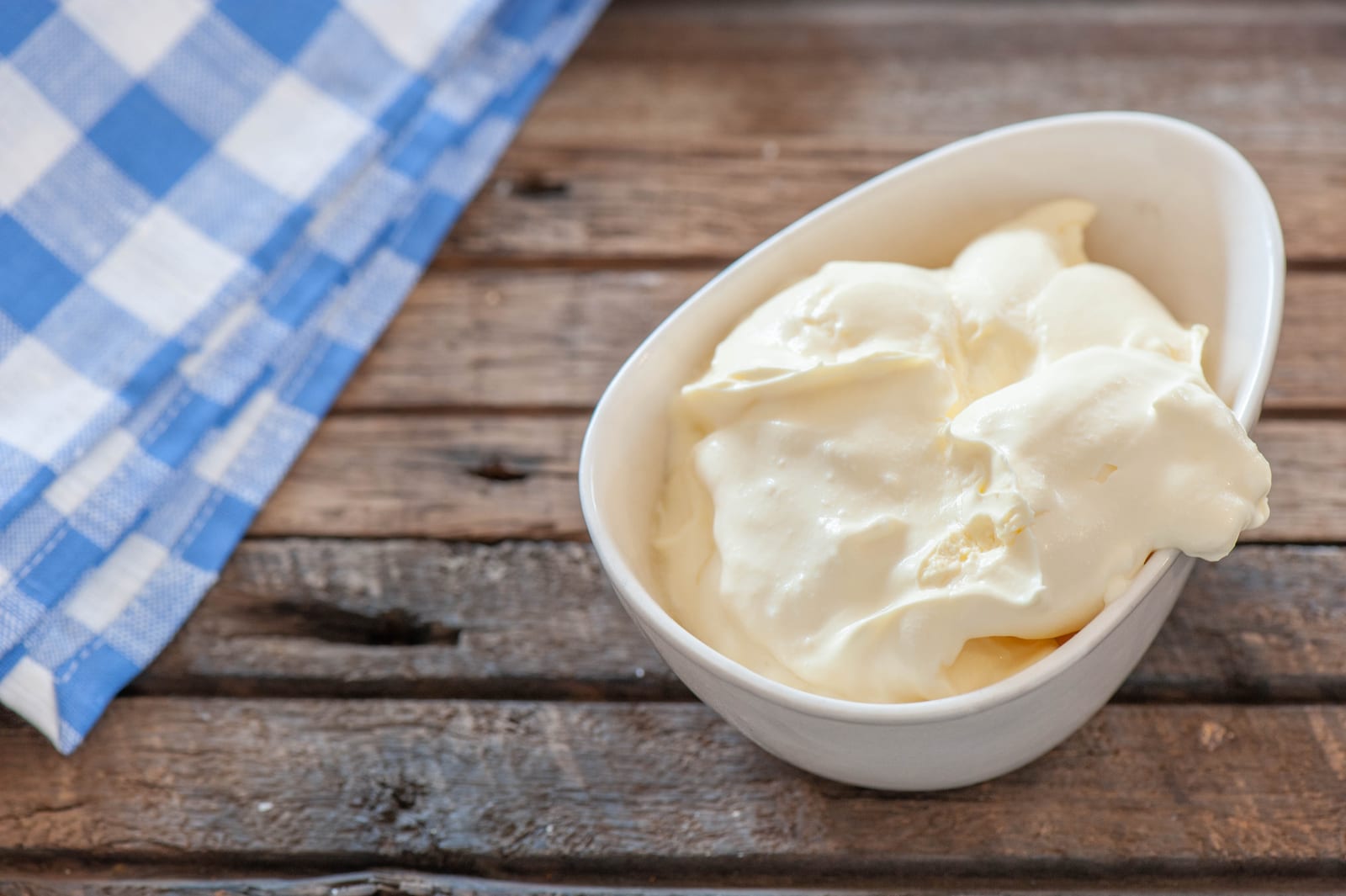 Thick sour cream spooned into a white bowl on a wooden table.