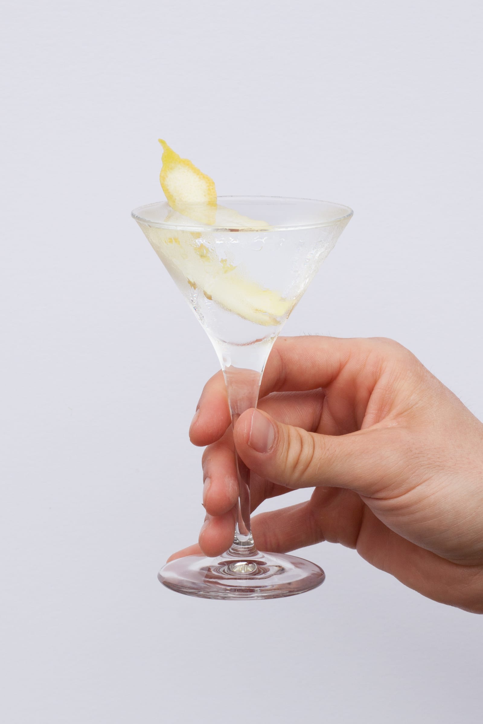 A hand holding a clear vodka martini garnished with a bright lemon twist.