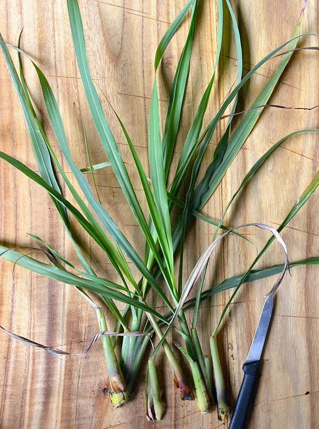 Fresh lemongrass stalks and leaves arranged on a wooden work surface beside a knife.