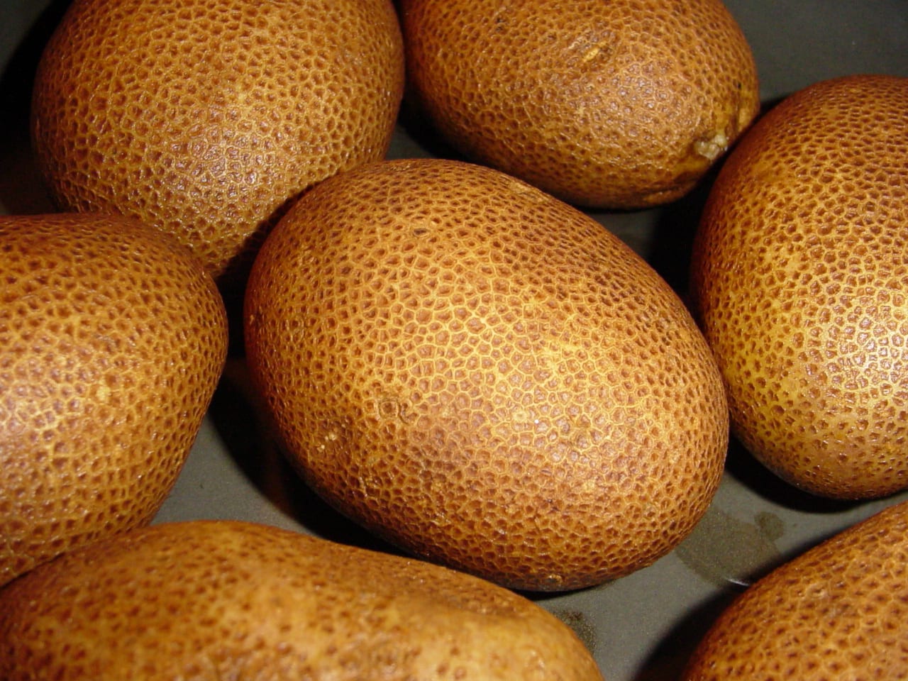 Several whole brown Russet Burbank potatoes grouped closely on a dark surface.
