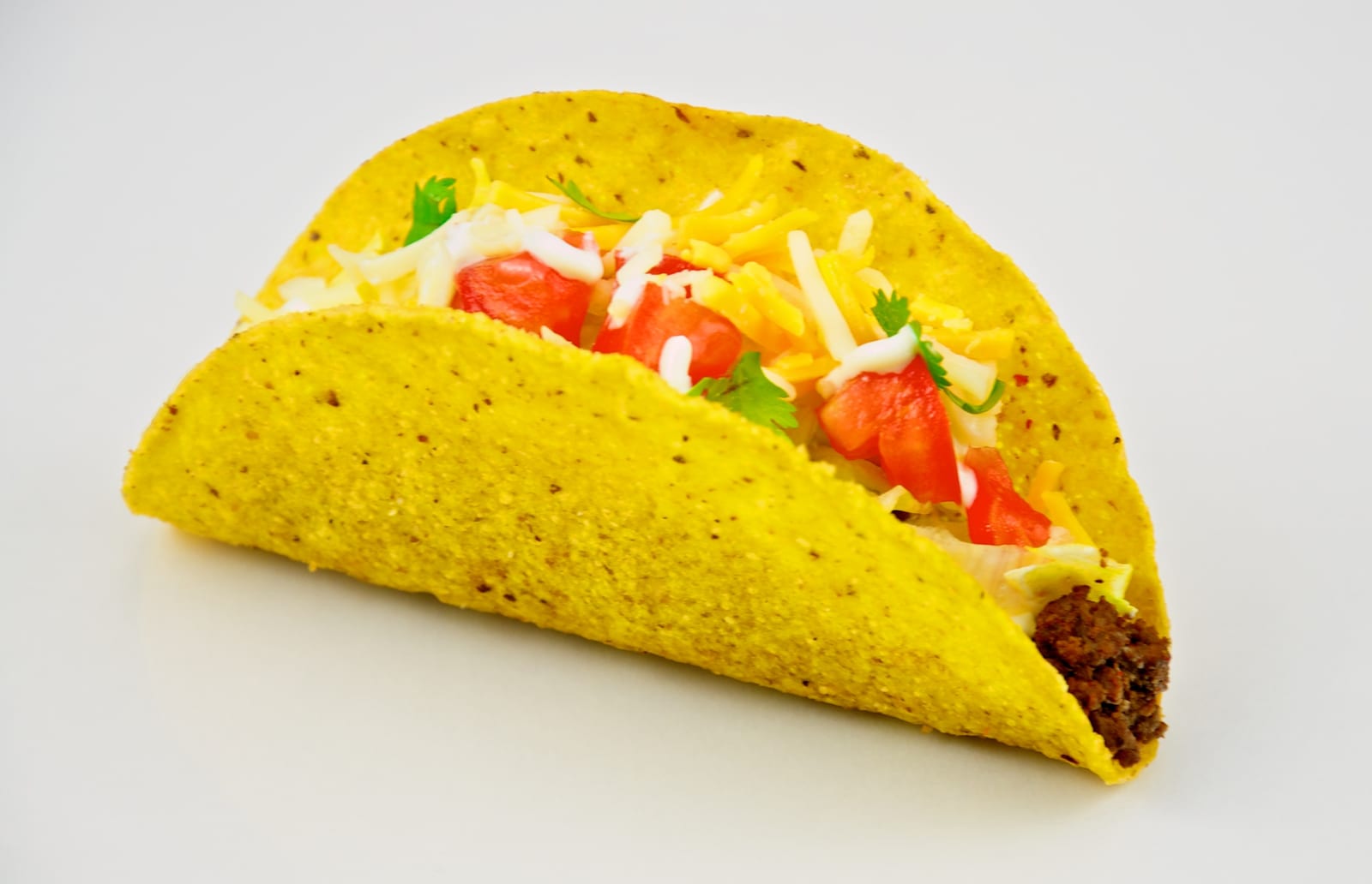 Two crisp yellow taco shells filled with ground beef, cheese, tomato, lettuce, and sour cream on a white surface.