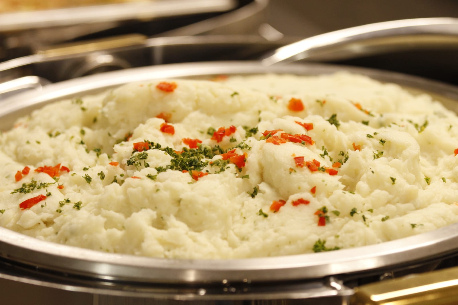 A shallow catering pan filled with creamy mashed potatoes and scattered herbs.