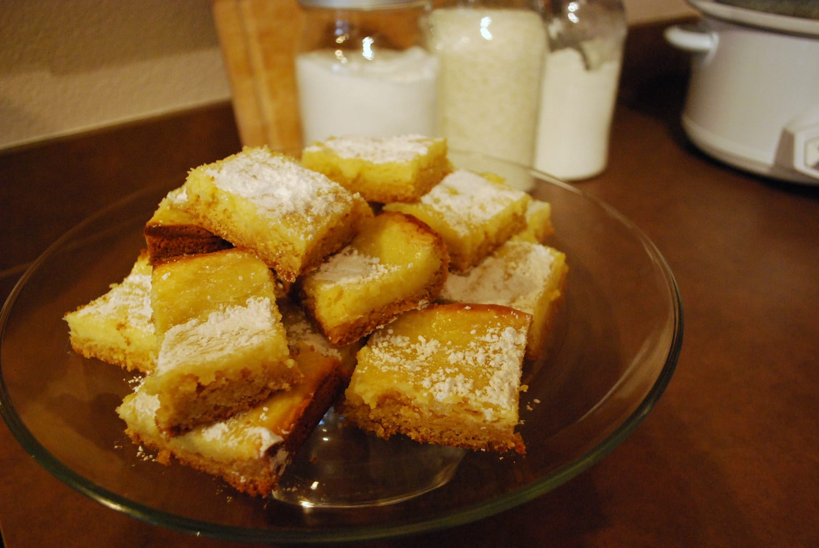 A pile of small golden gooey butter cake squares dusted with powdered sugar.