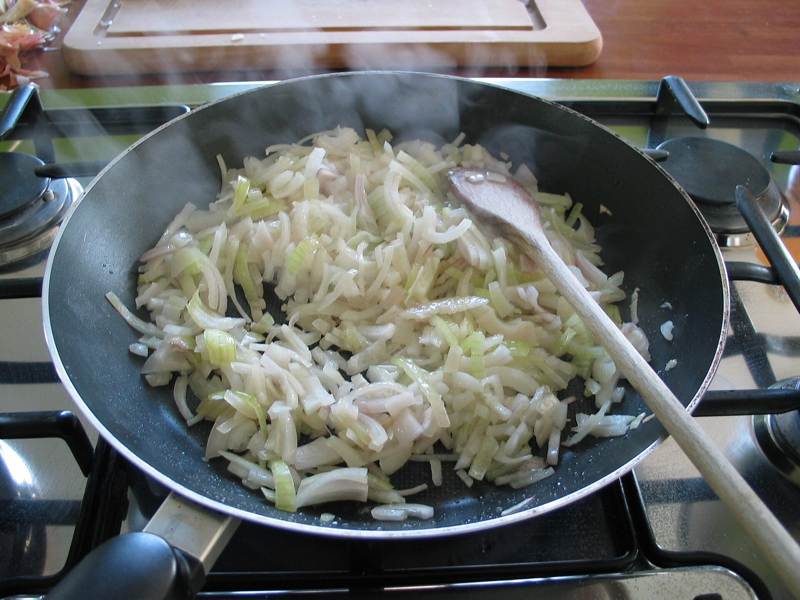Thinly sliced onions softening in a black frying pan with steam rising.