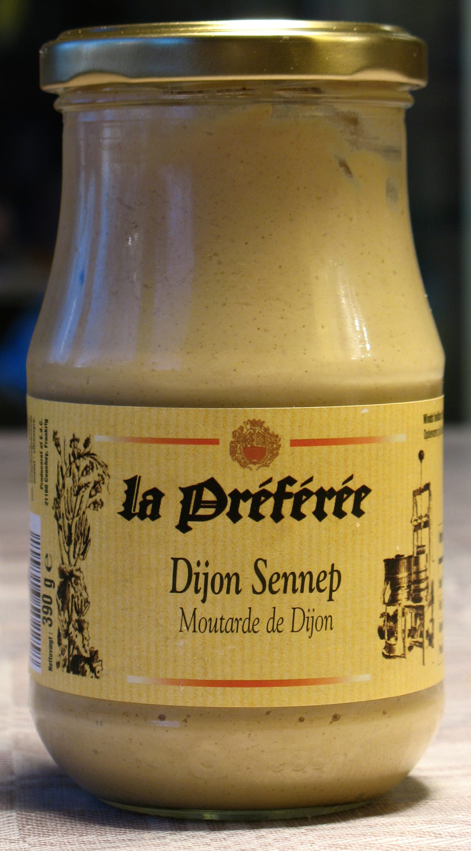 A glass jar of pale Dijon mustard with a cream paper label.