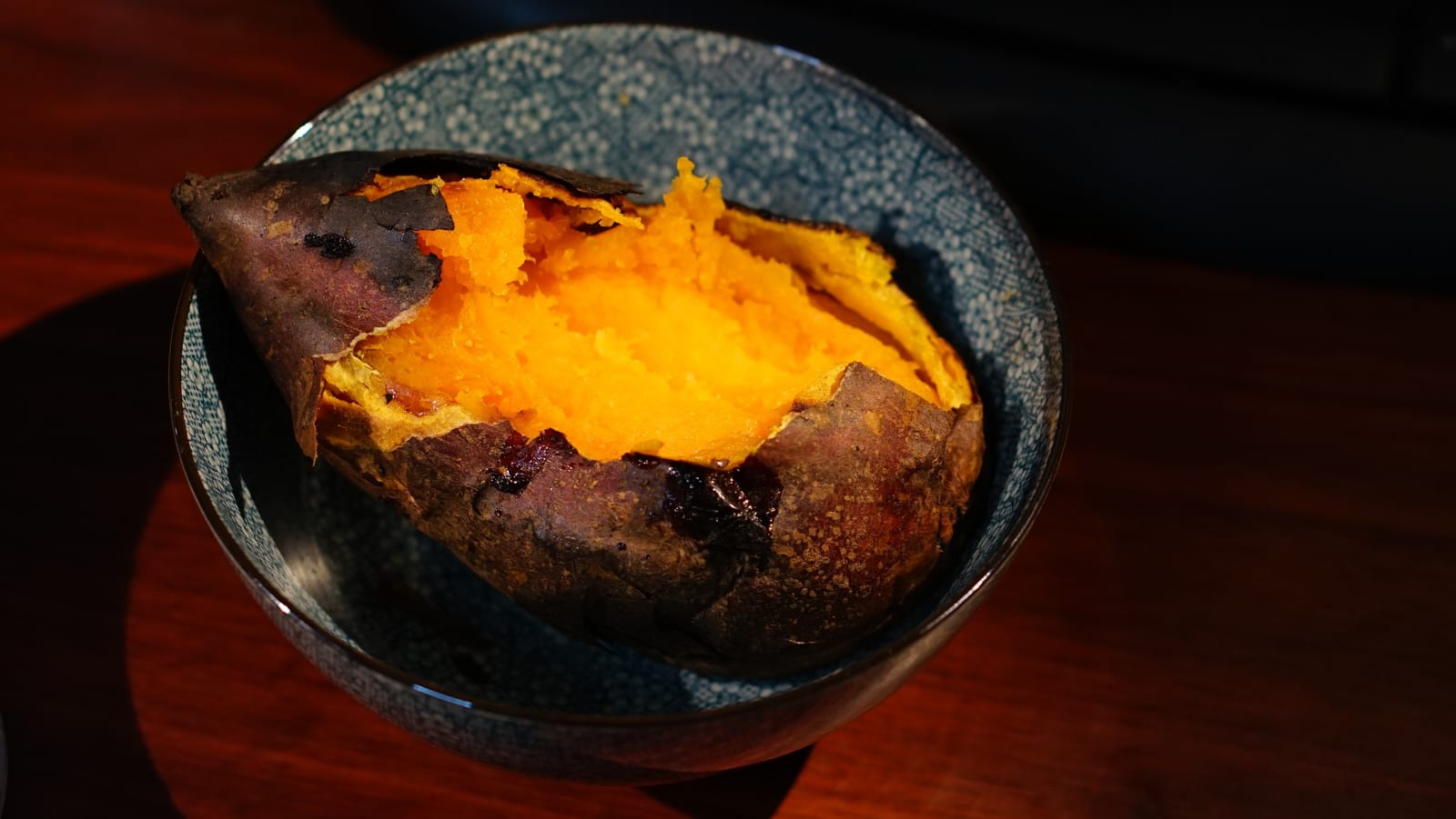 A roasted orange-fleshed sweet potato opened in a blue ceramic bowl.