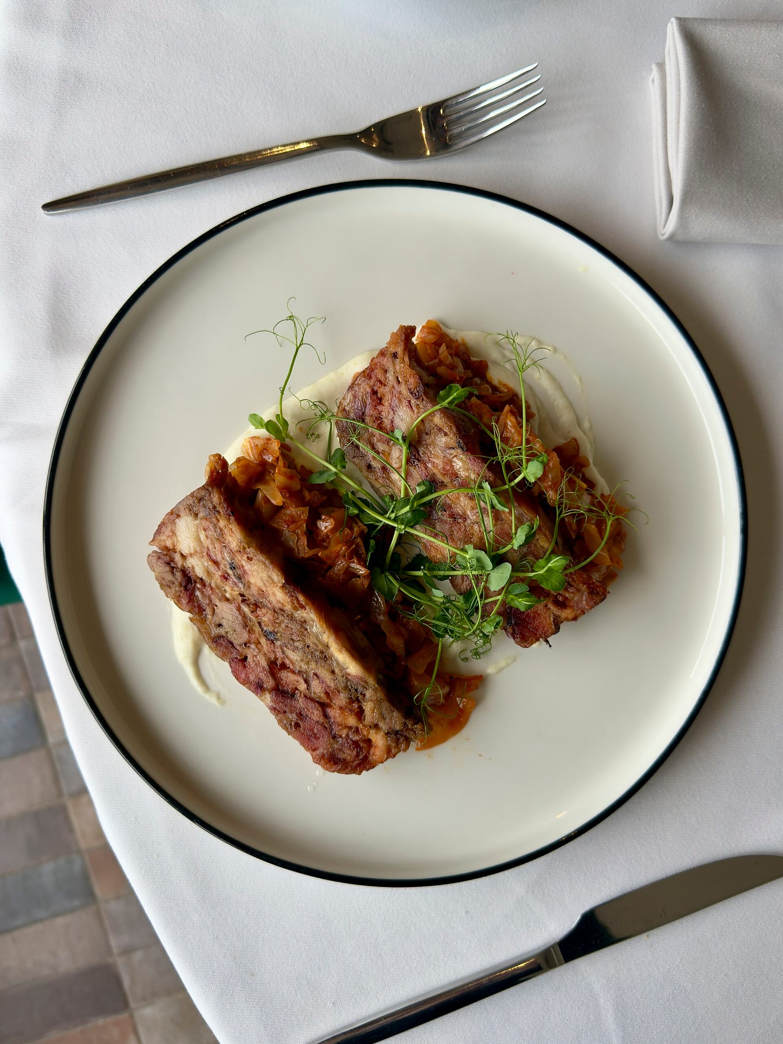A restaurant-style plate of sliced meatloaf with sauce, herbs, linen, and polished silverware.