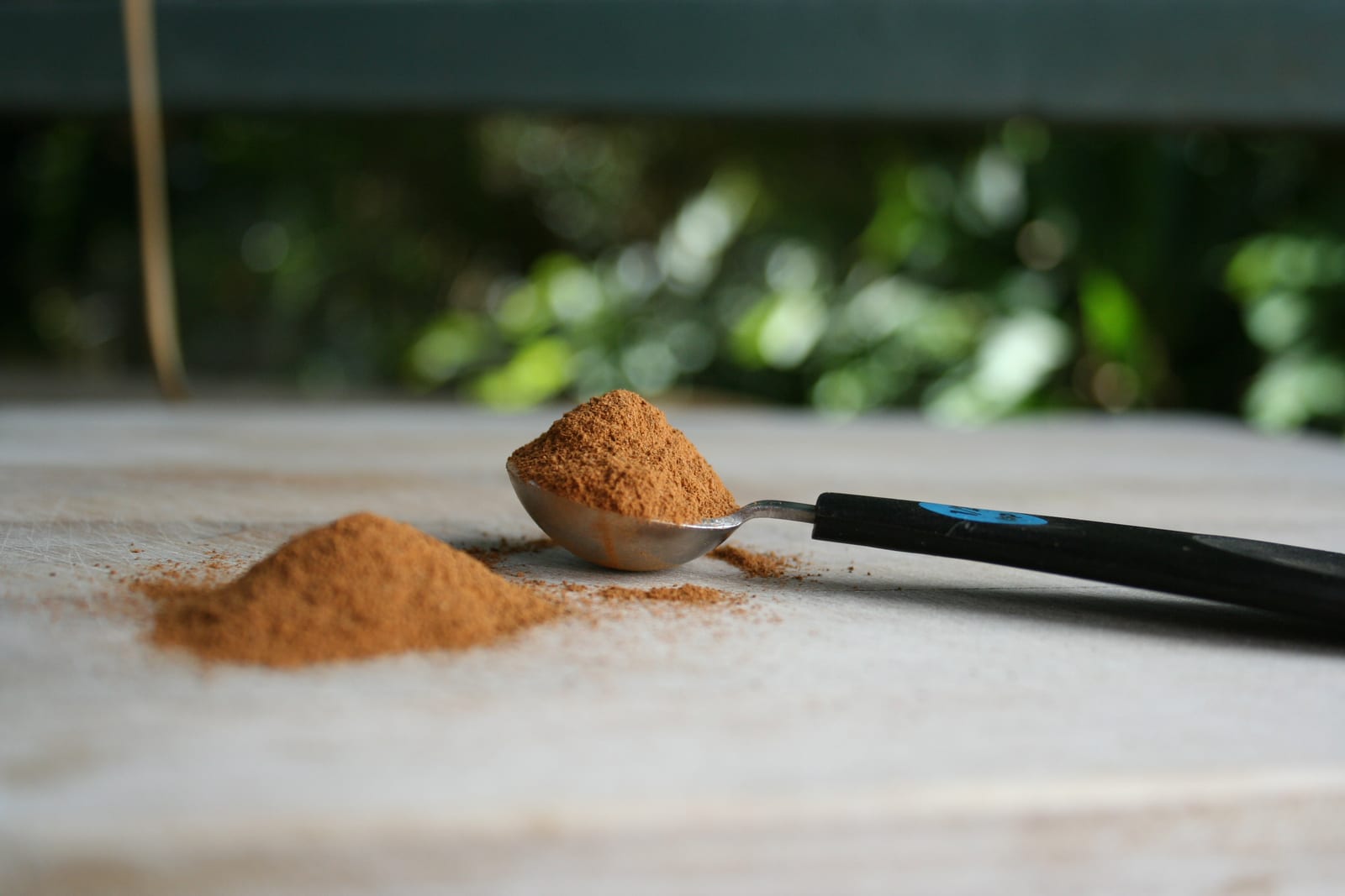 Ground cinnamon mounded in a measuring spoon on a stone surface.
