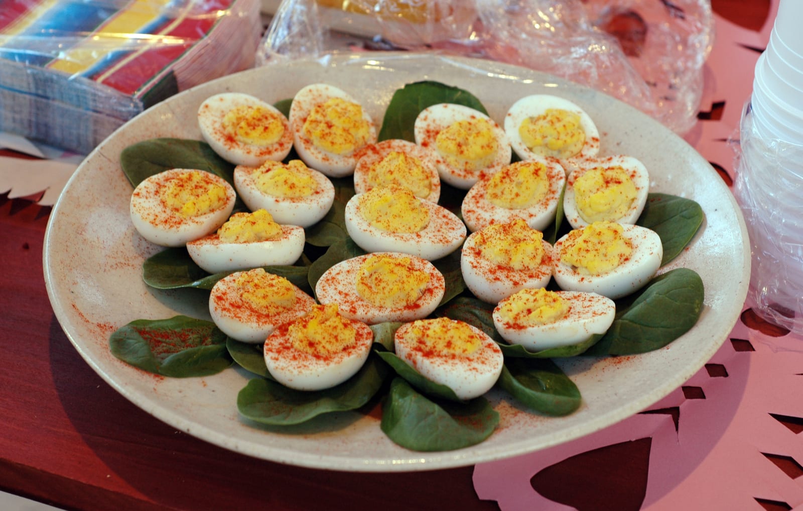 A large party platter of paprika-dusted deviled eggs arranged over spinach leaves.