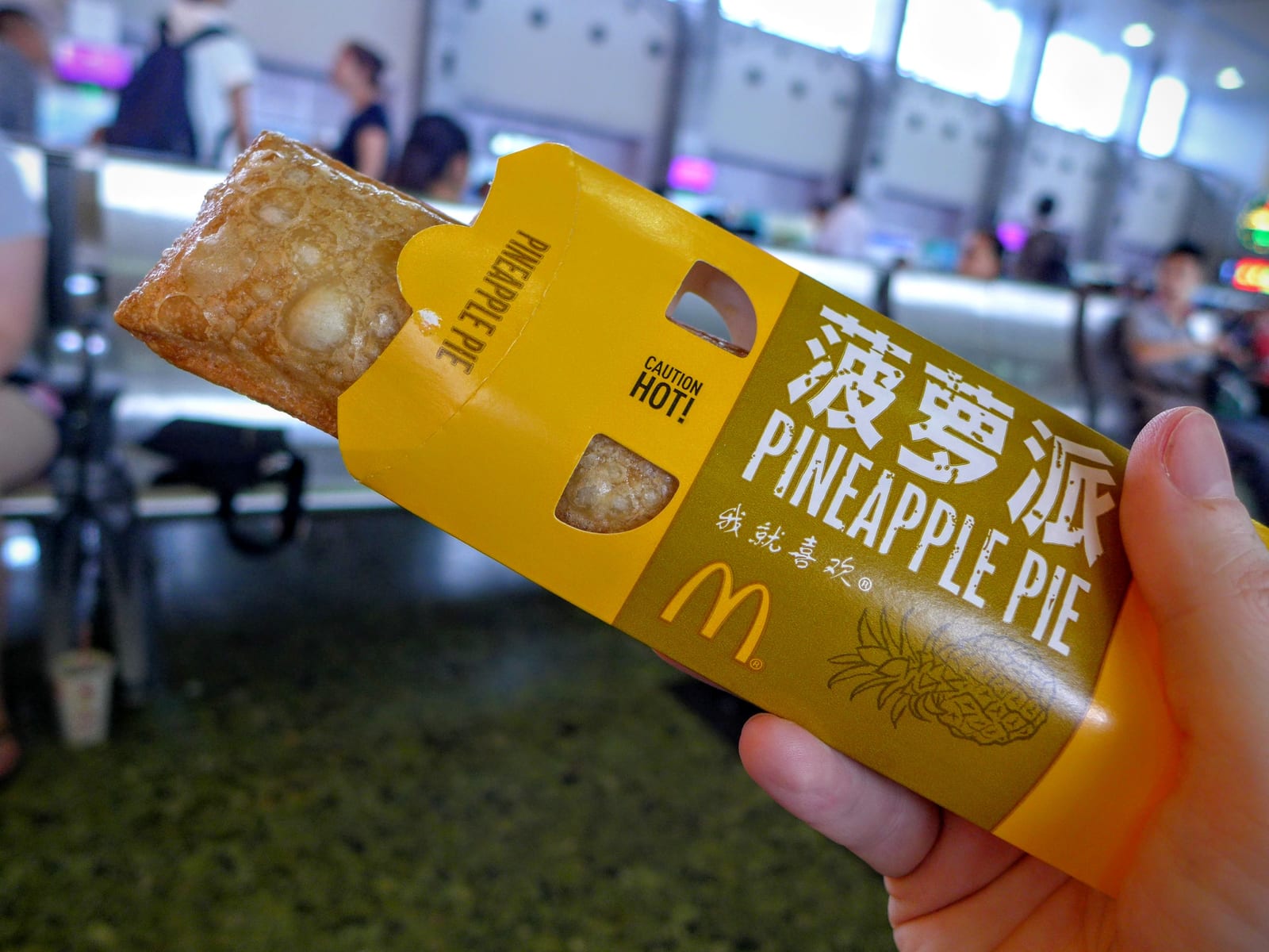 A rectangular golden fried pineapple pie resting on its opened paper sleeve.
