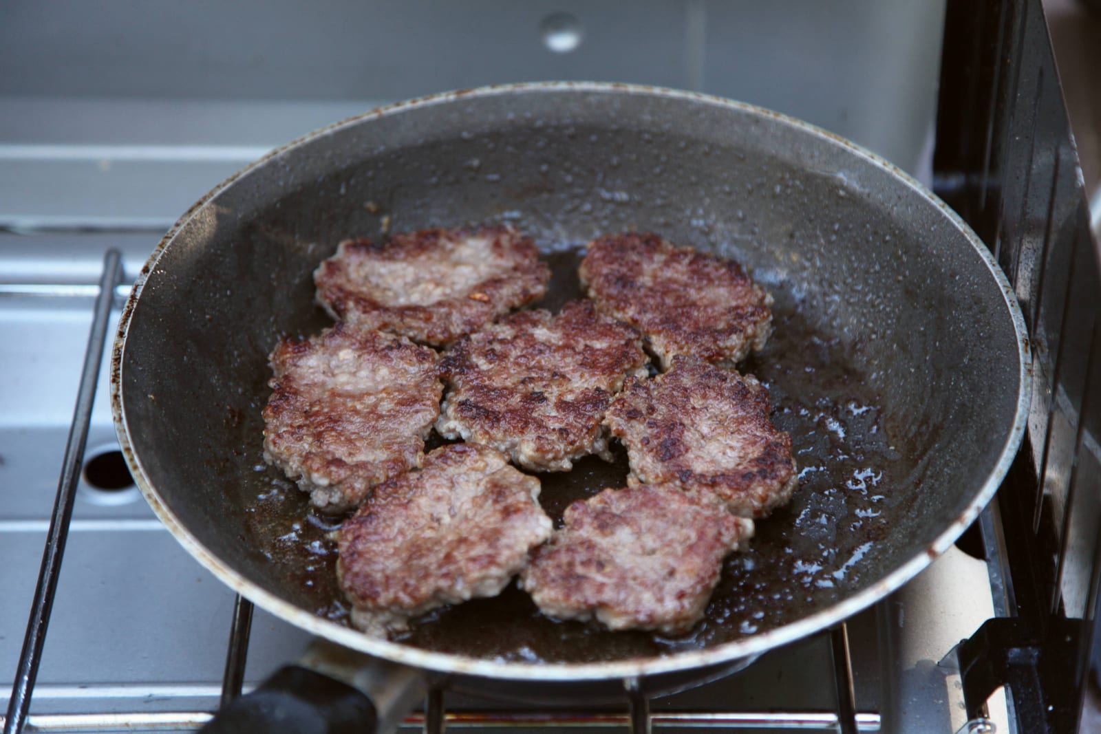 Breakfast sausage patties browning in a wide skillet.