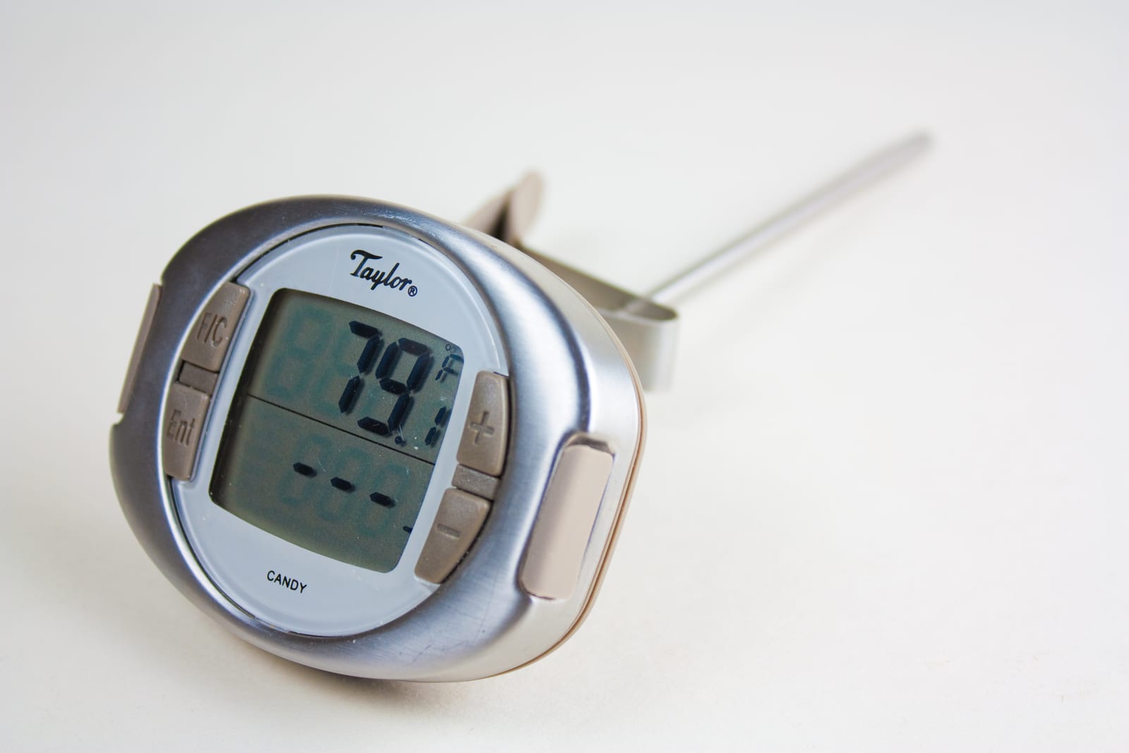 A digital candy thermometer with a long metal probe on a white surface.