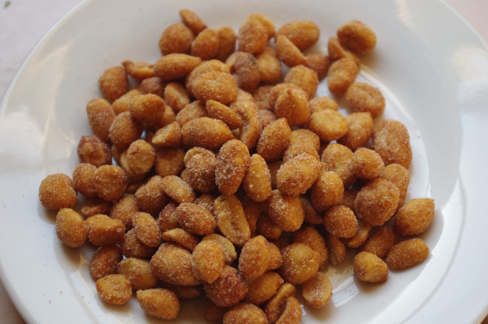 Honey-roasted peanuts coated in a fine golden sugar crust on a white plate.