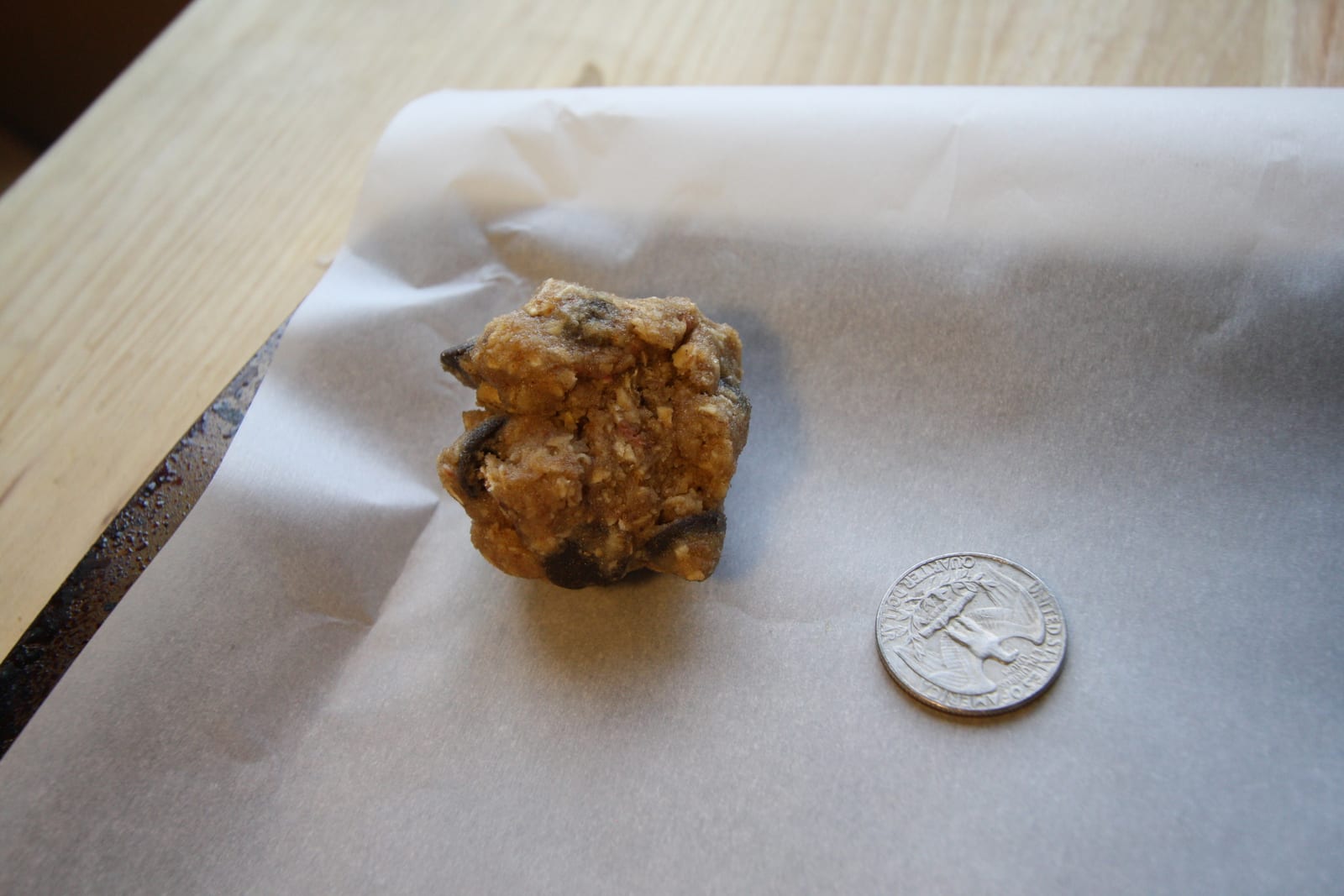 A small scoop of oatmeal chocolate chip cookie dough on a lined baking sheet.