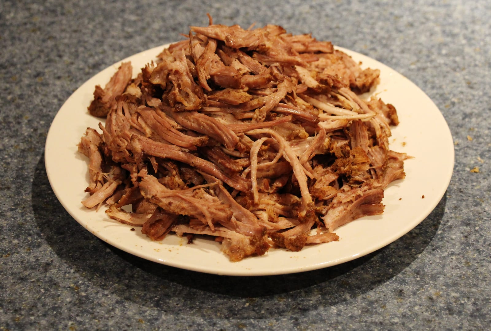 A mound of freshly pulled pork shoulder with long tender strands on a white plate.