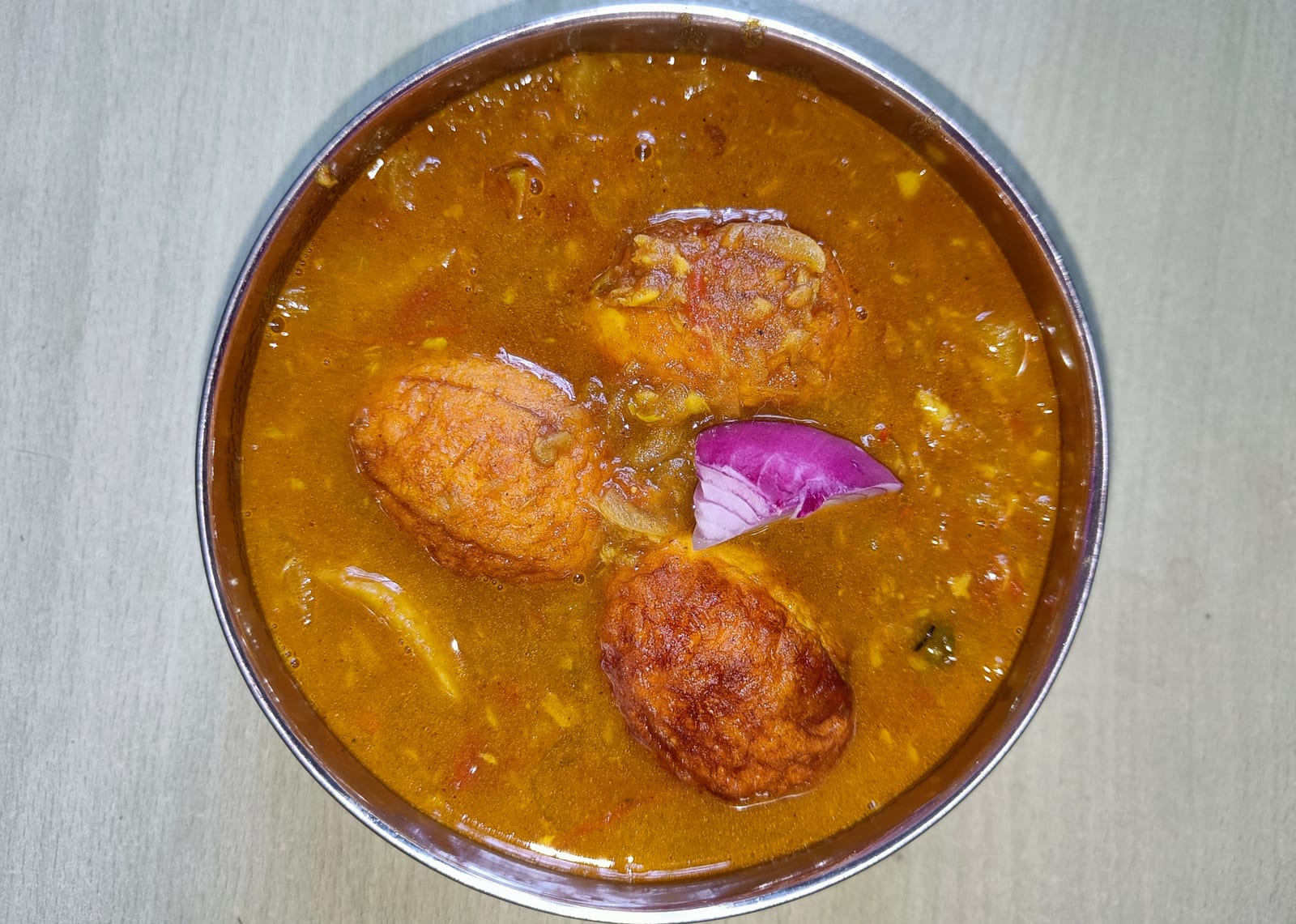 Halved boiled eggs in a red-brown Indian curry sauce with herbs.