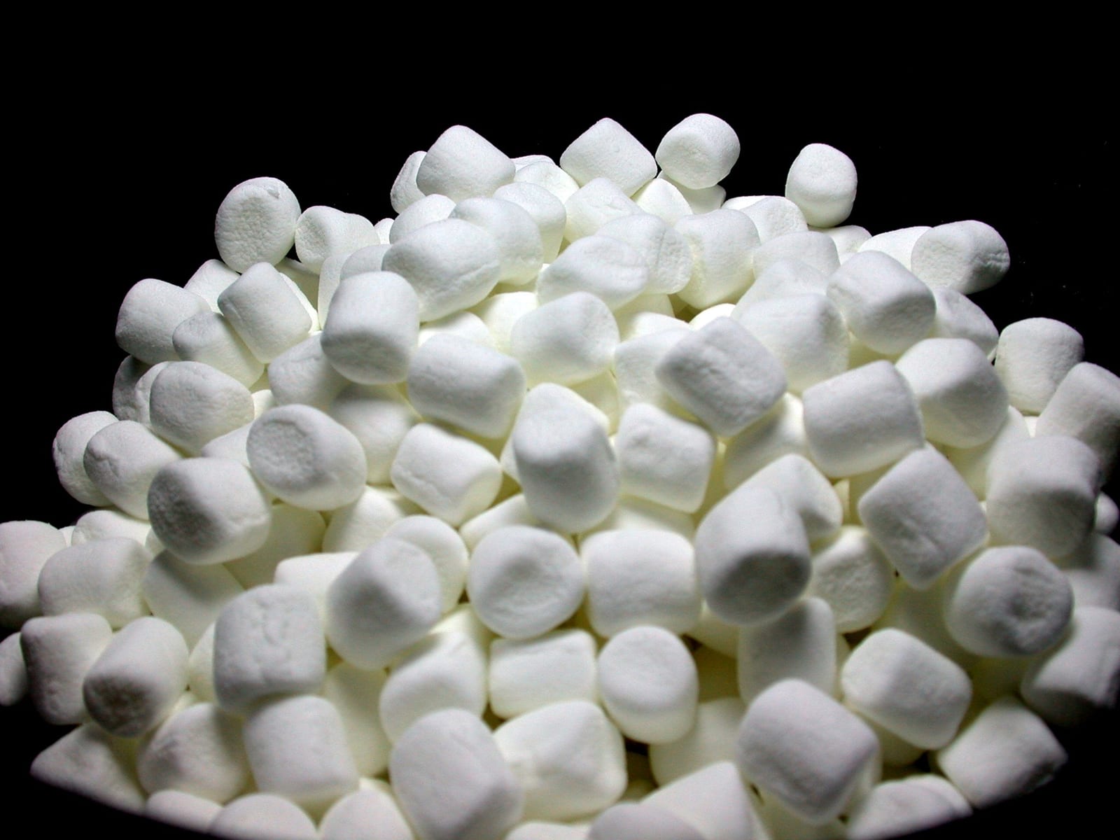 A mound of white miniature marshmallows against a black background.