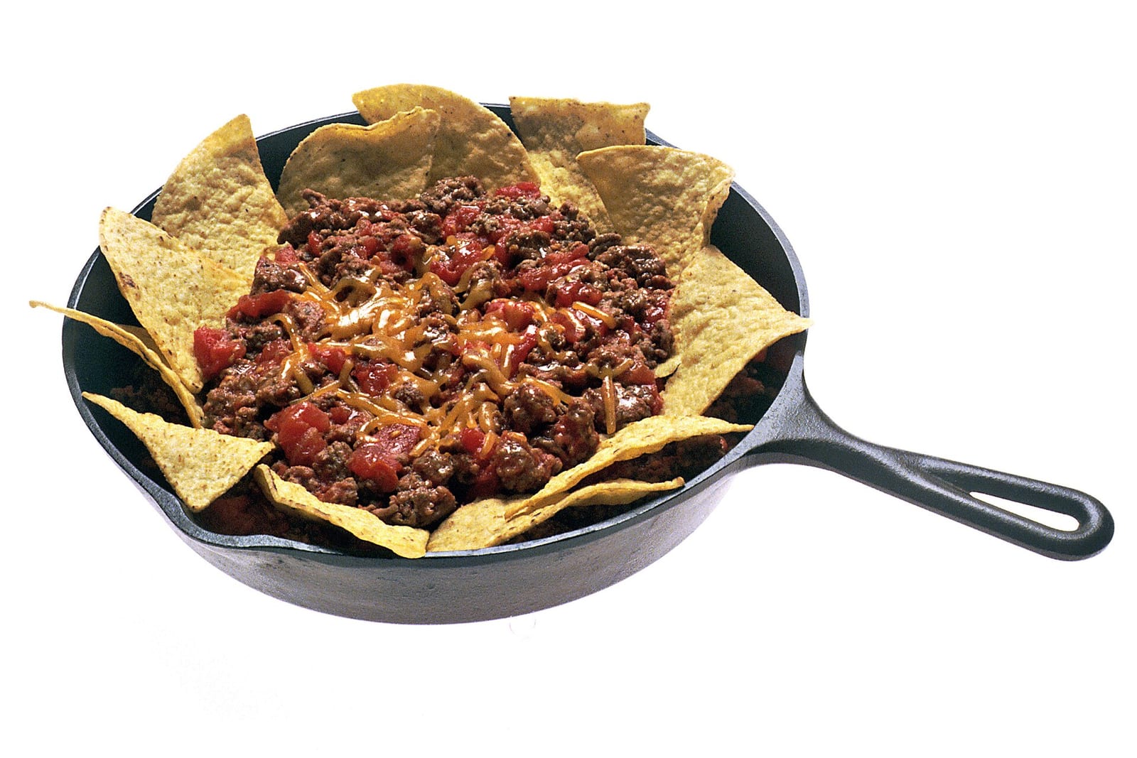 Tortilla chips arranged around seasoned beef, beans, tomatoes, and melted cheddar in a cast-iron skillet.