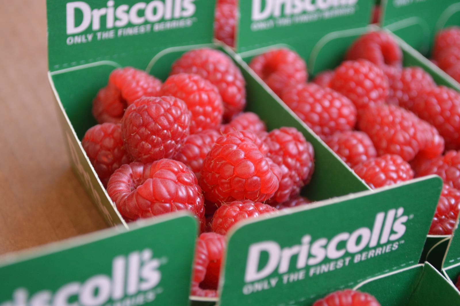 Fresh red raspberries packed closely in green market cartons.