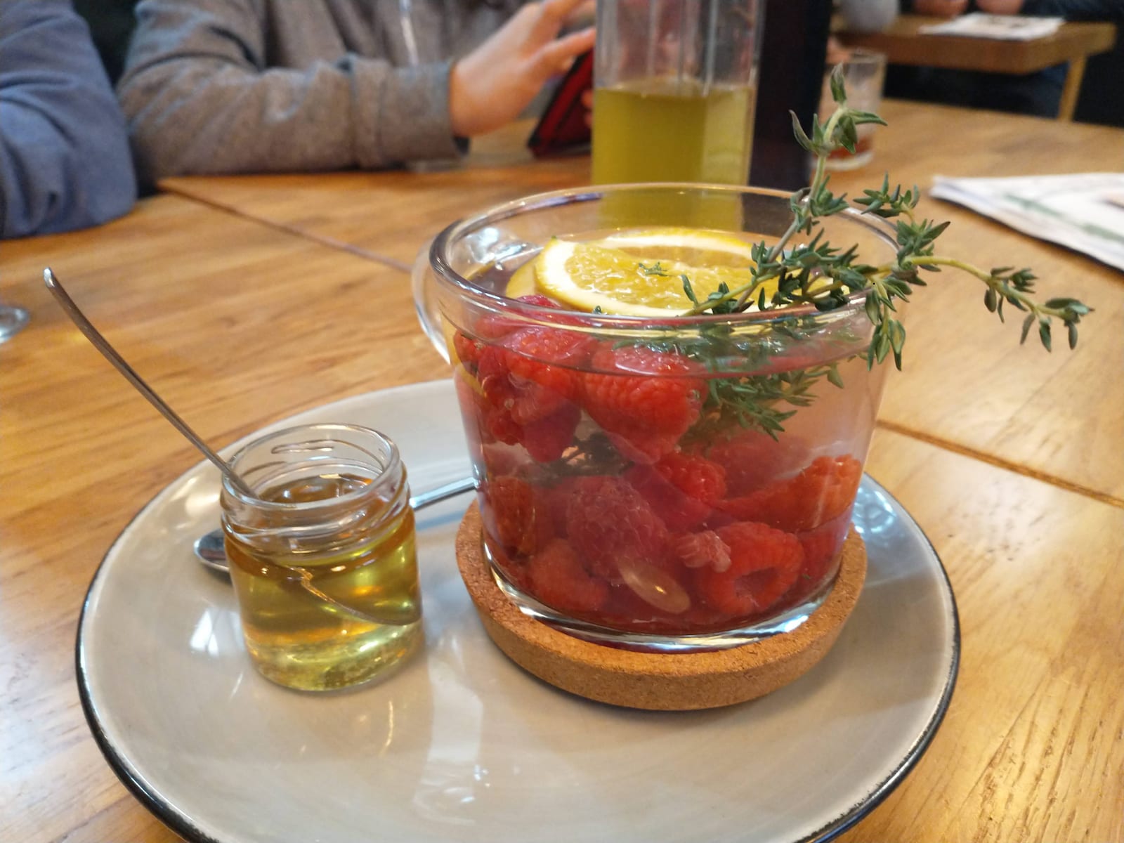 Raspberry tea in a clear cup with a small jar of honey and spoon alongside.