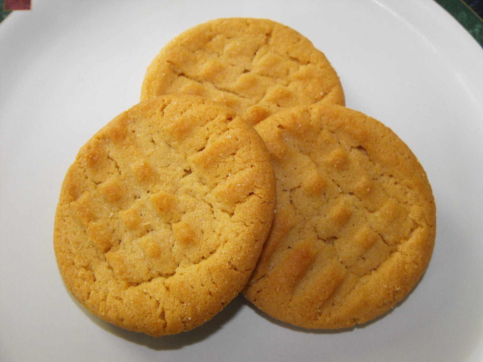 Three golden peanut butter cookies overlapping on a white plate.