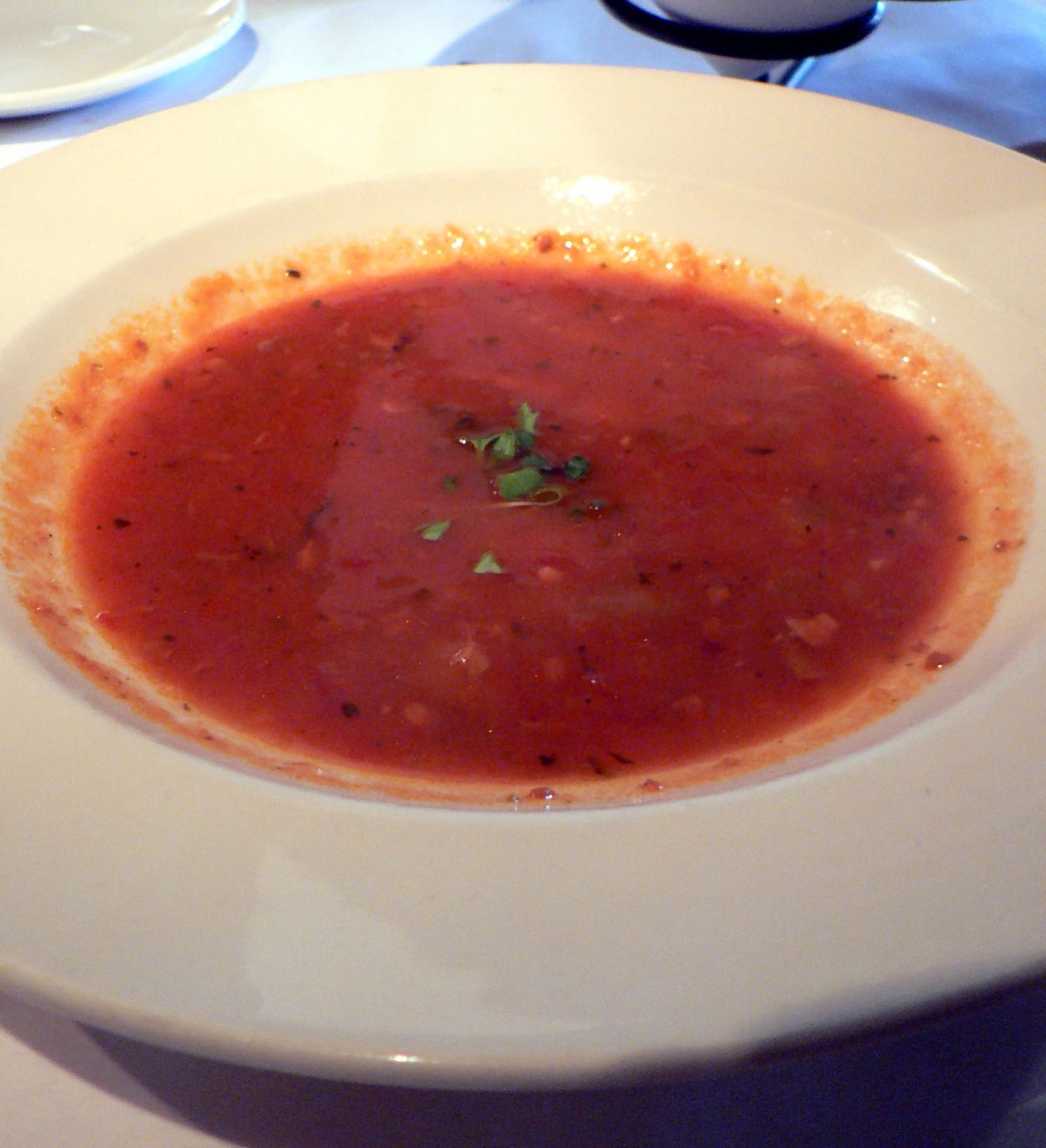 A shallow white bowl filled with red tomato-based clam chowder and a small herb garnish.