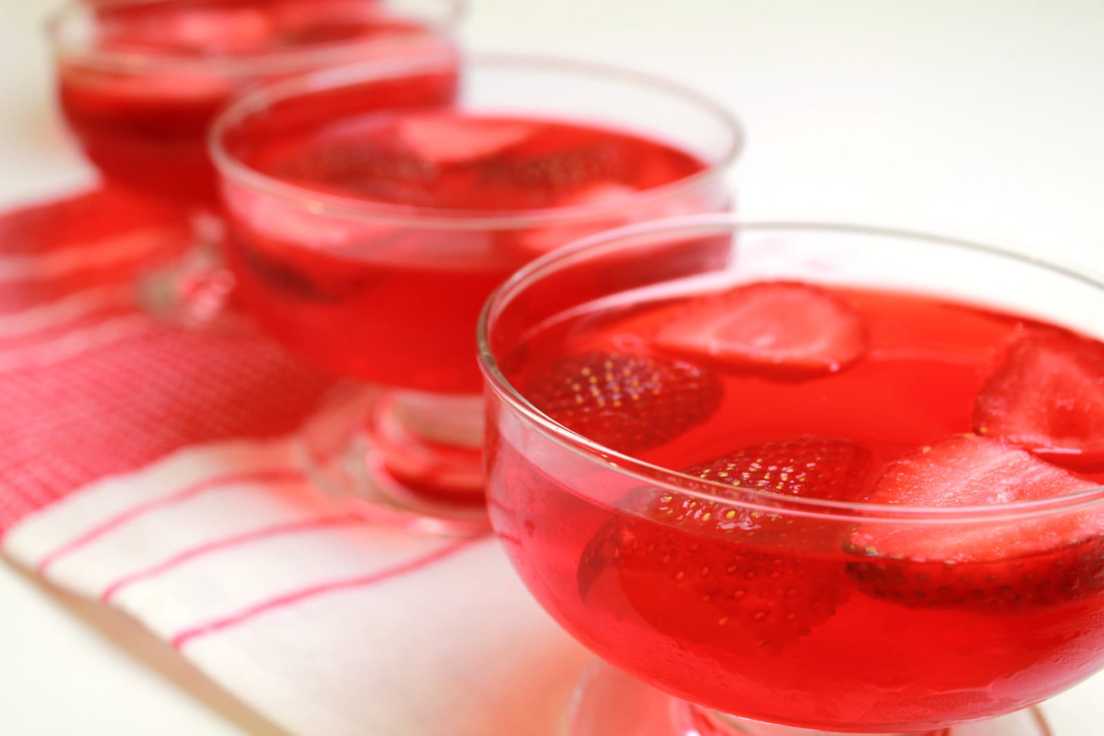 Clear red strawberry jelly with whole and sliced strawberries in glass dessert bowls.