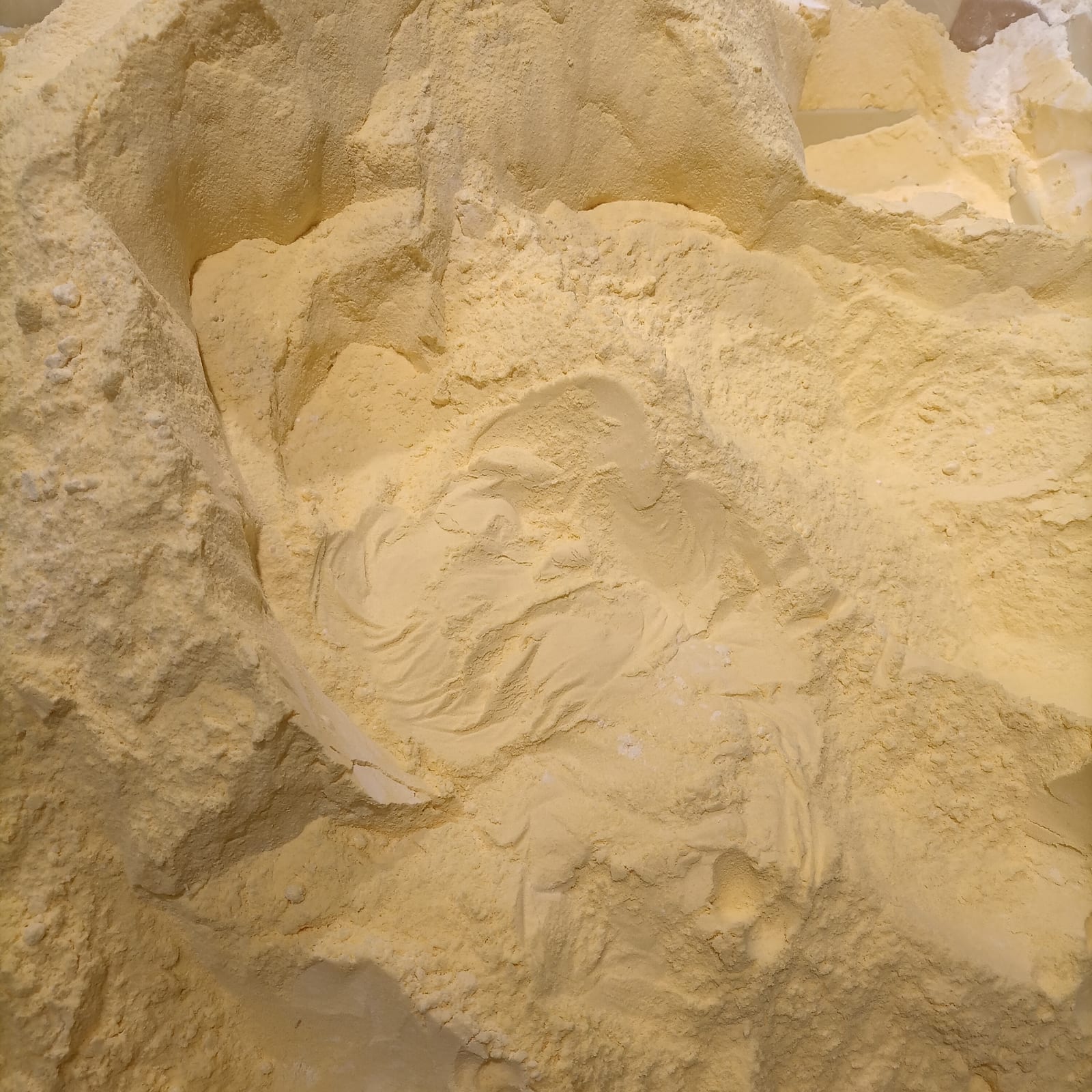 Fine yellow corn flour gathered in a shallow wooden bowl.