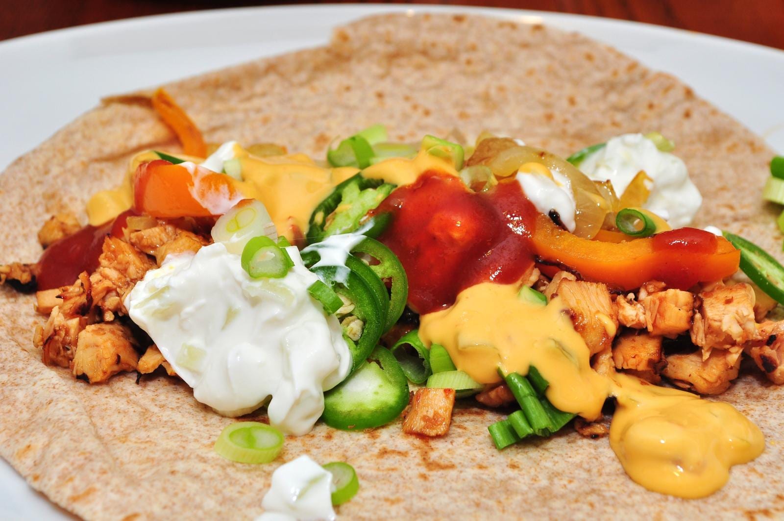Chopped chicken, orange pepper, jalapeño, scallions, salsa, and sour cream on a flour tortilla.