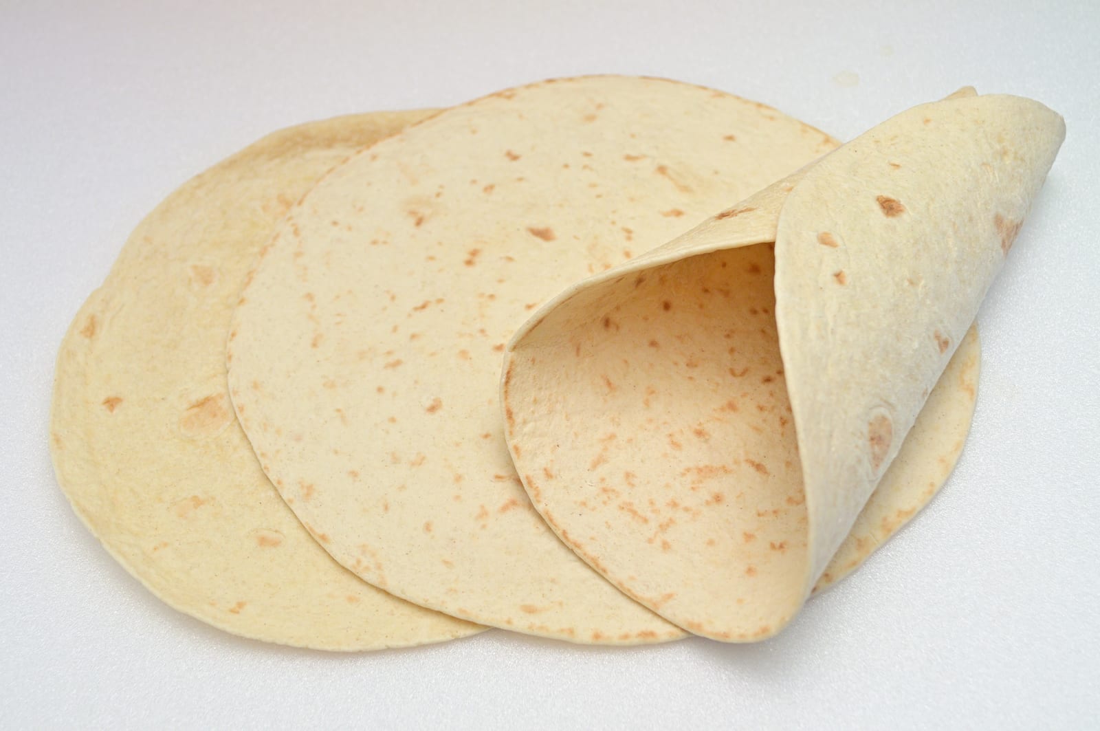 A stack of pale flour tortillas with softly browned spots and one edge folded upward.