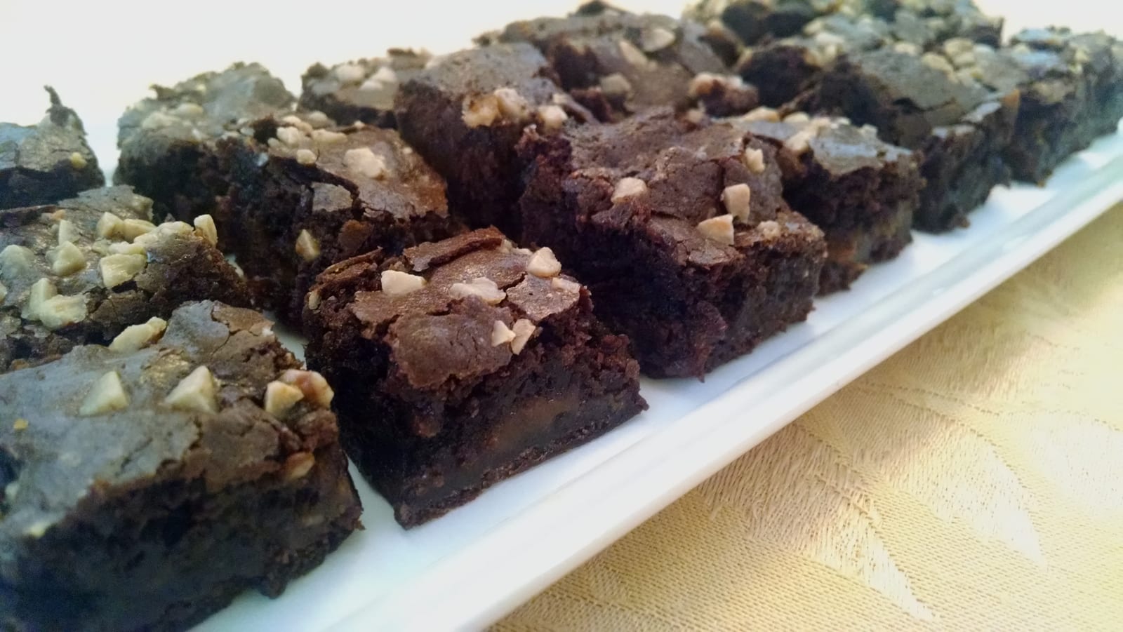 Small dark chocolate brownie squares arranged closely on a white platter.