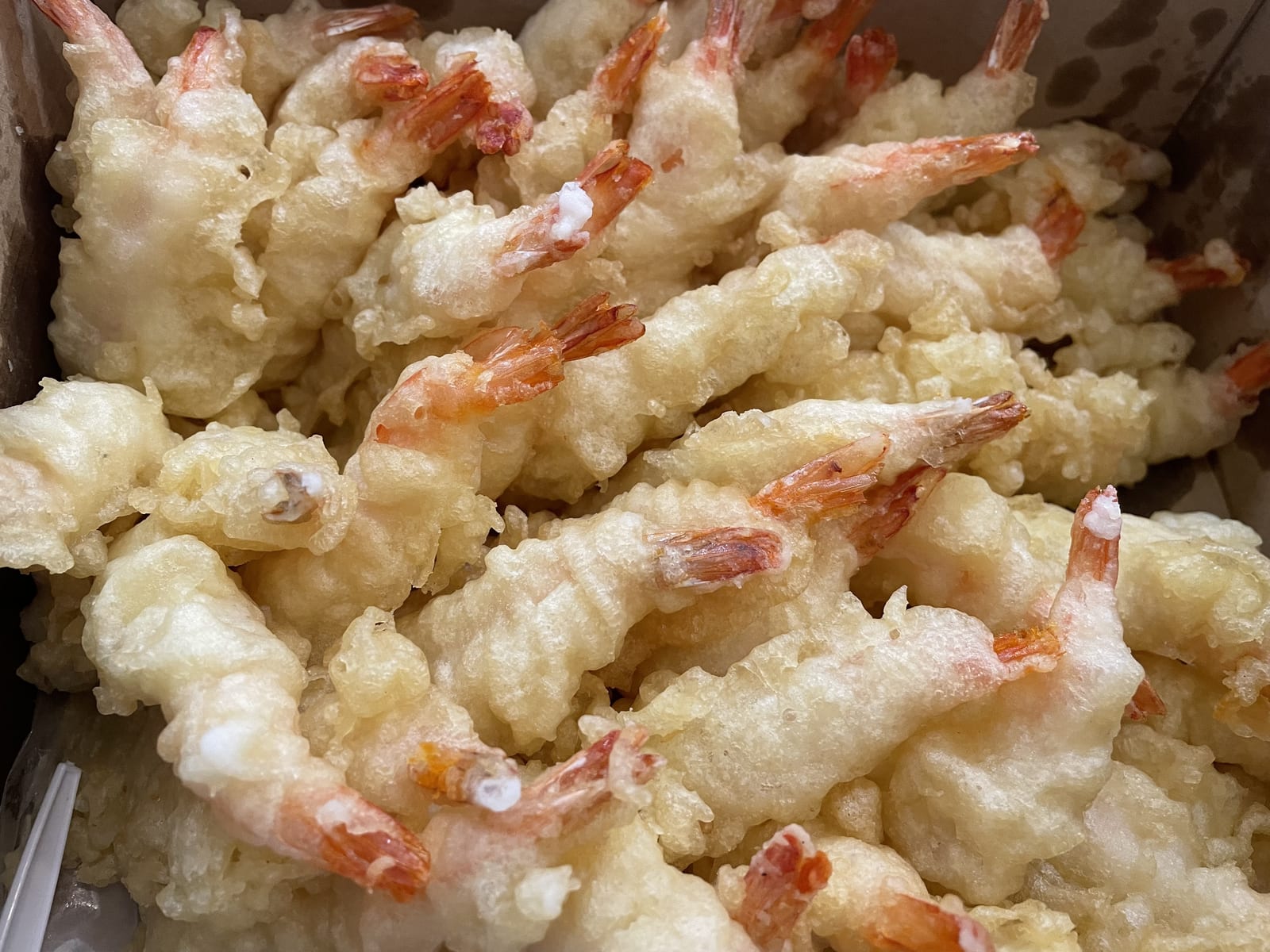 A close view of tail-on shrimp in a pale, airy fried batter.
